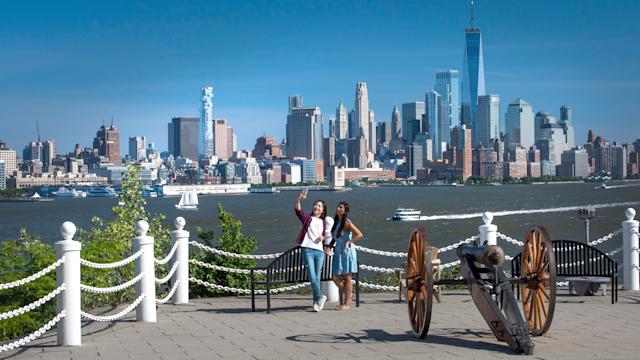 Two students pose for a selfie at Castle Point with a view of the New York Skyline.