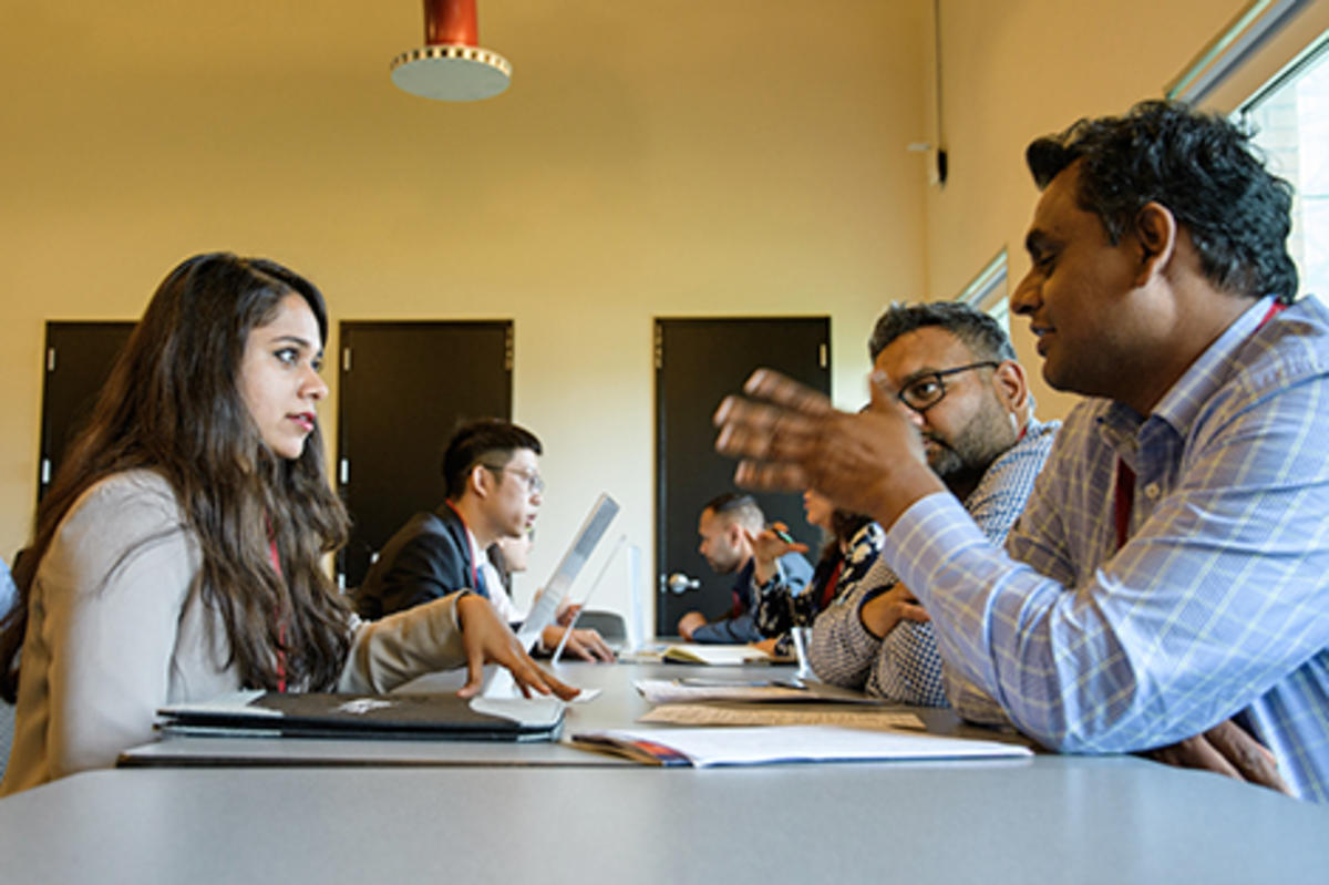 A female student listens to a make recruiter at a conference table on campus.