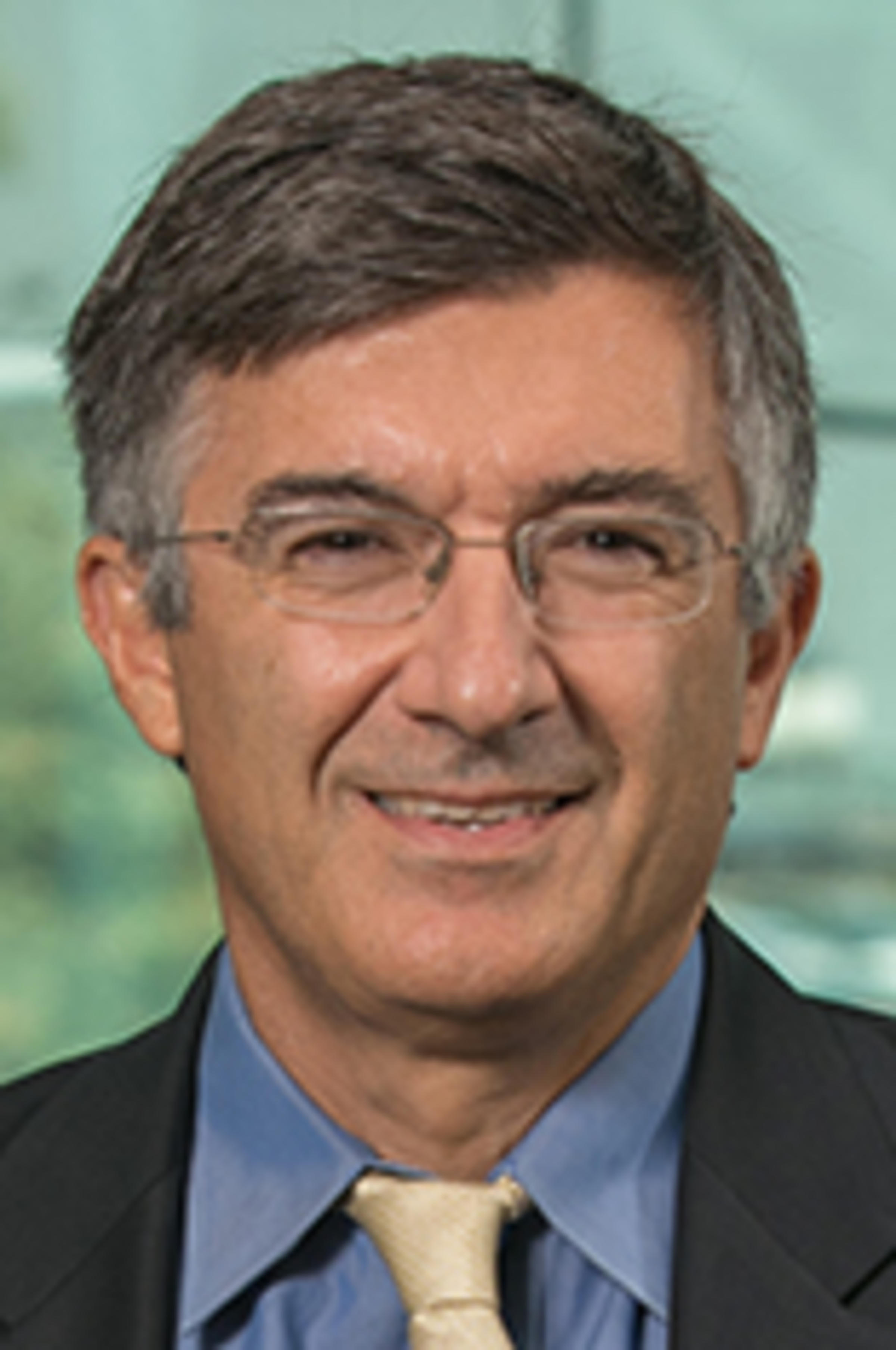 Headshot of Alkis Vazacopoulos in a dark suit against the Manhattan skyline.