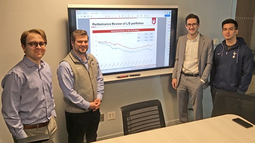 Four students show the dashboard they created while standing in a conference room at the high-tech Hanlon Lab.
