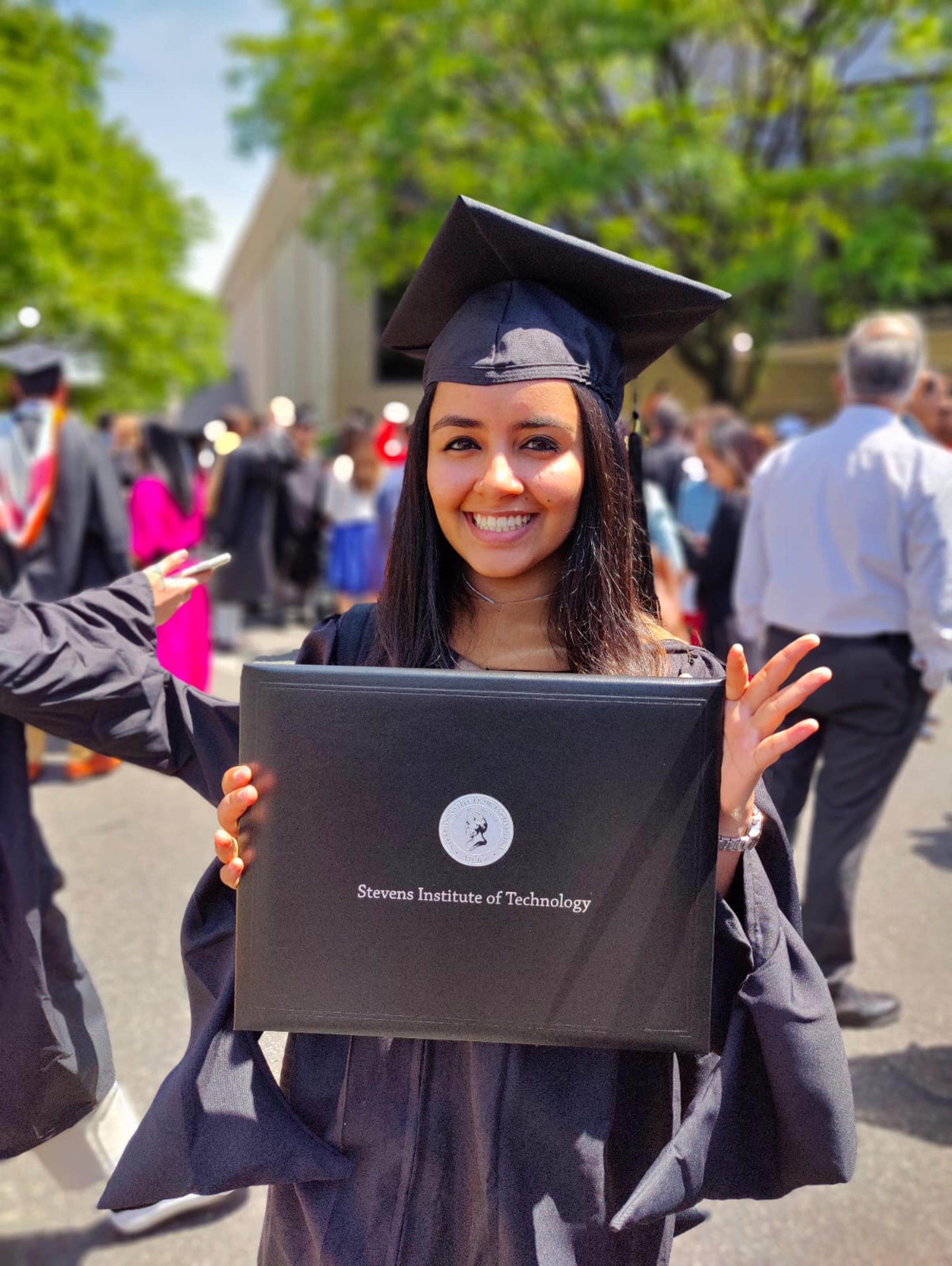 Rhythm Goyal holds her Stevens Institute of Technology diploma wearing her cap and gown.