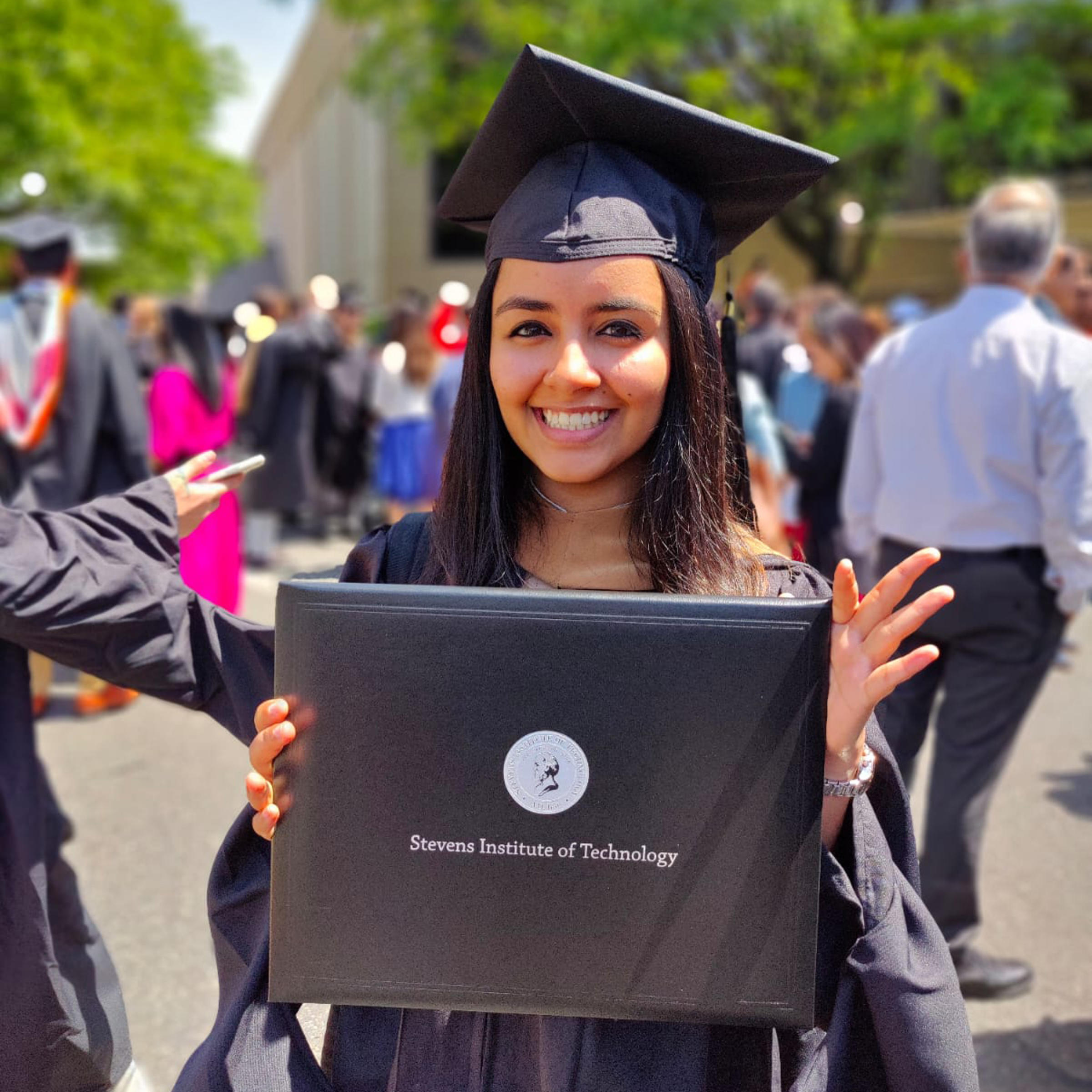 Rhythm Goyal holds her Stevens Institute of Technology diploma wearing her cap and gown.