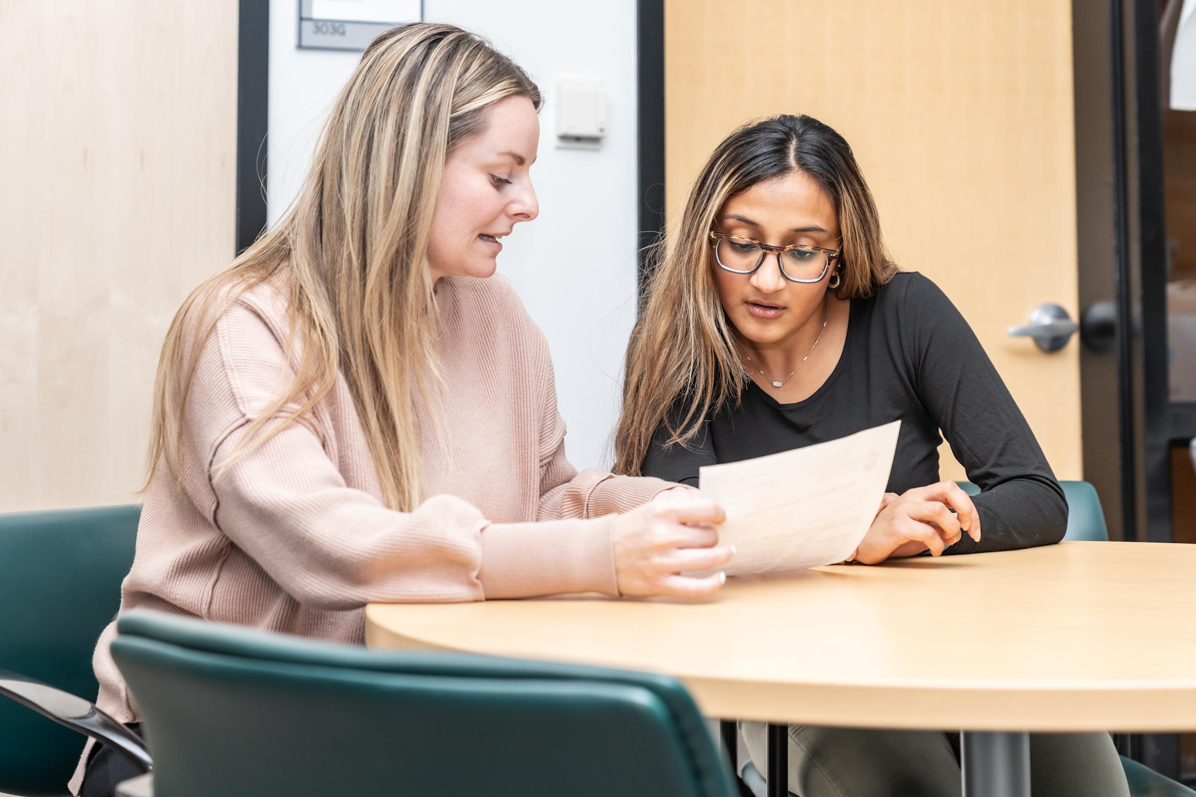 Serena Shah sits at a table with Amy Katzenback who is showing her something on a sheet of paper.
