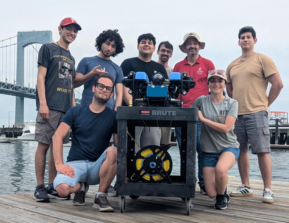 A group of students, including Ivana Collado Gonzalez and mentor Brendan Englot, posing for a photo with their underwater robot.