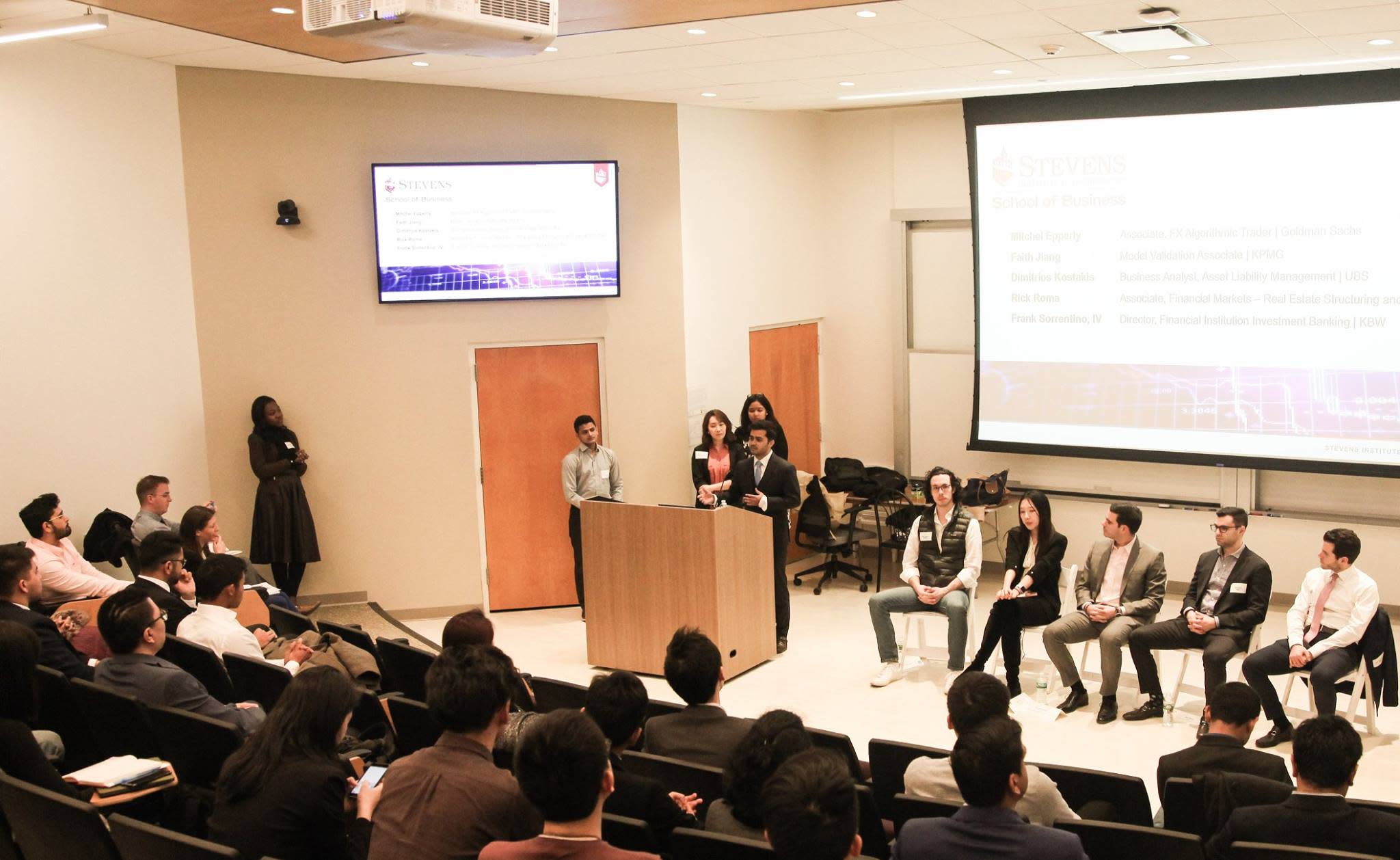 Himanshu Kumar stands behind a podium addressing a crowd while a panel of people sit behind him.