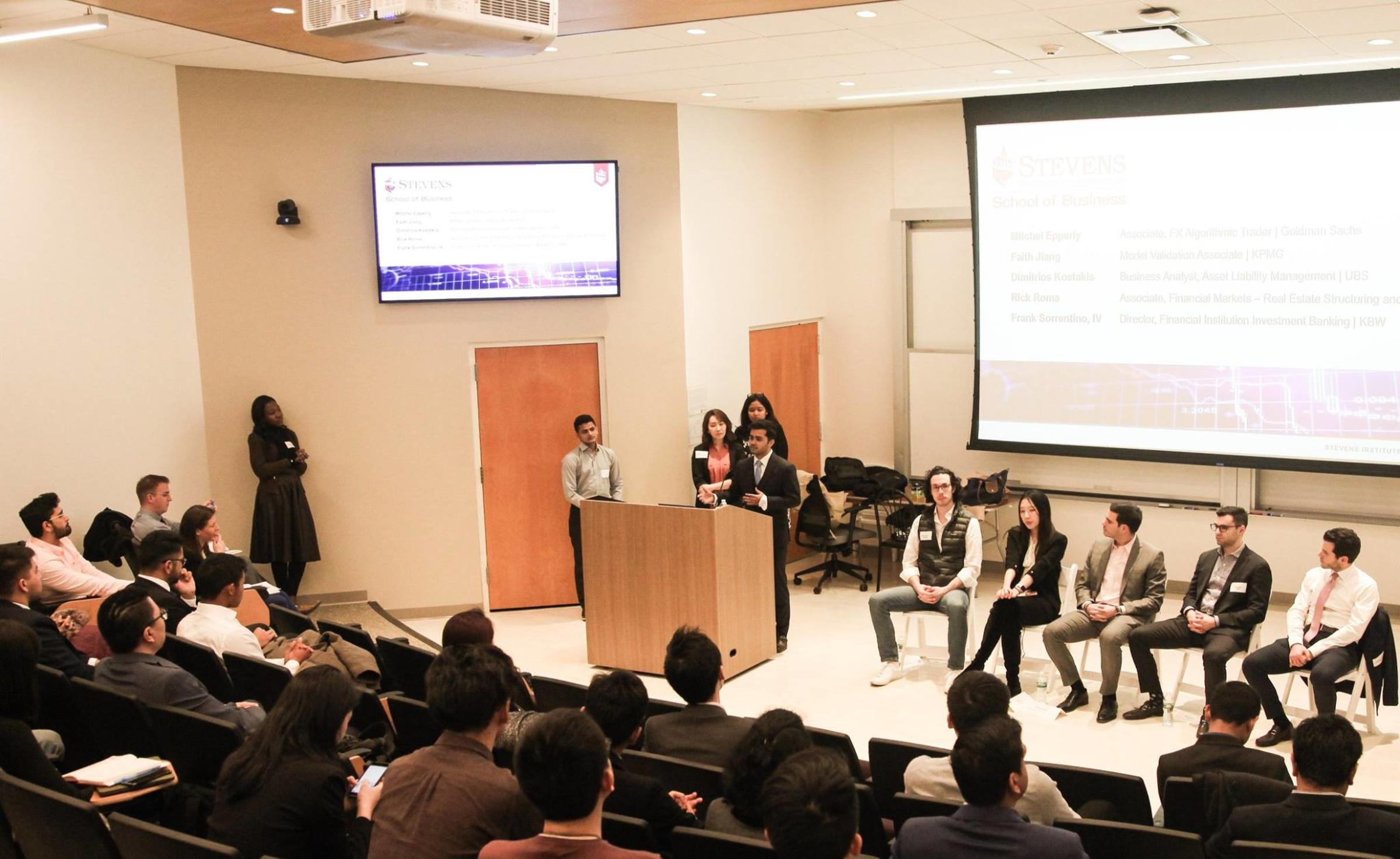 Himanshu Kumar stands behind a podium addressing a crowd while a panel of people sit behind him.