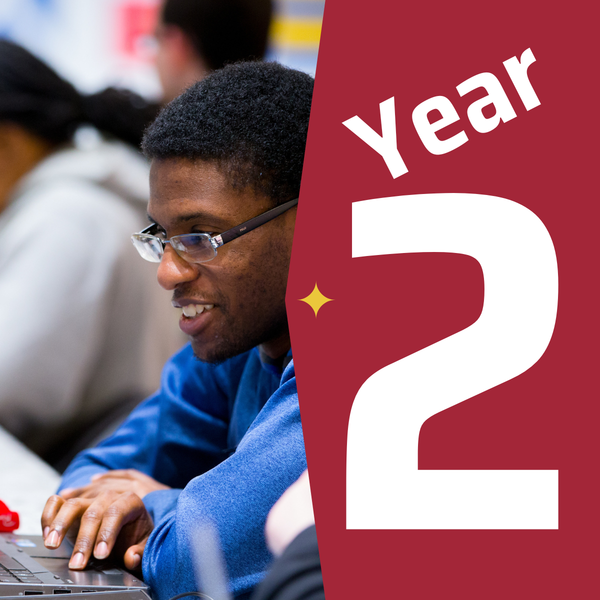 A student wearing a blue shirt sitting at a table in front of a laptop next to a graphic that says year two.