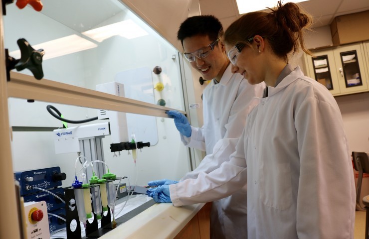 A photo of two students wearing lab gear looking at test tubes