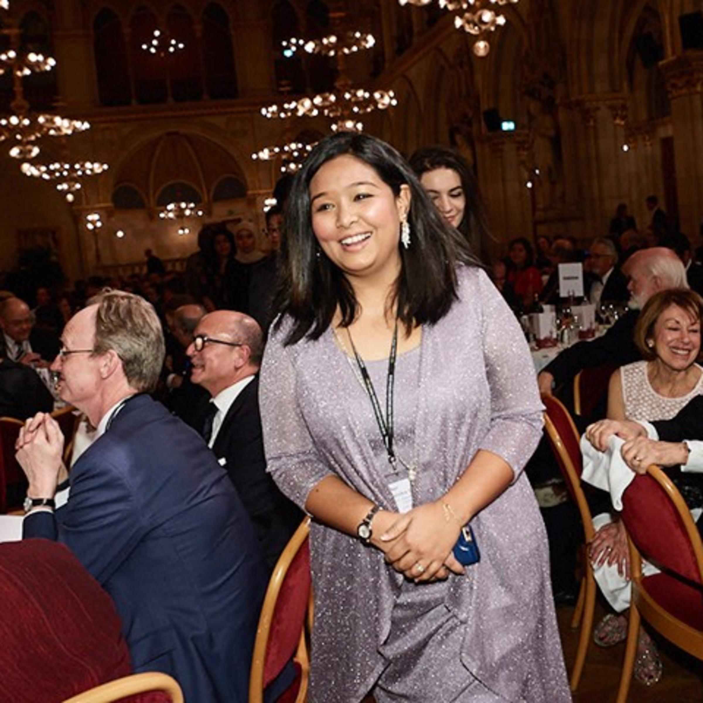 Kanika Ghocha walking to the stage in a ballroom filled with business and academic leaders.