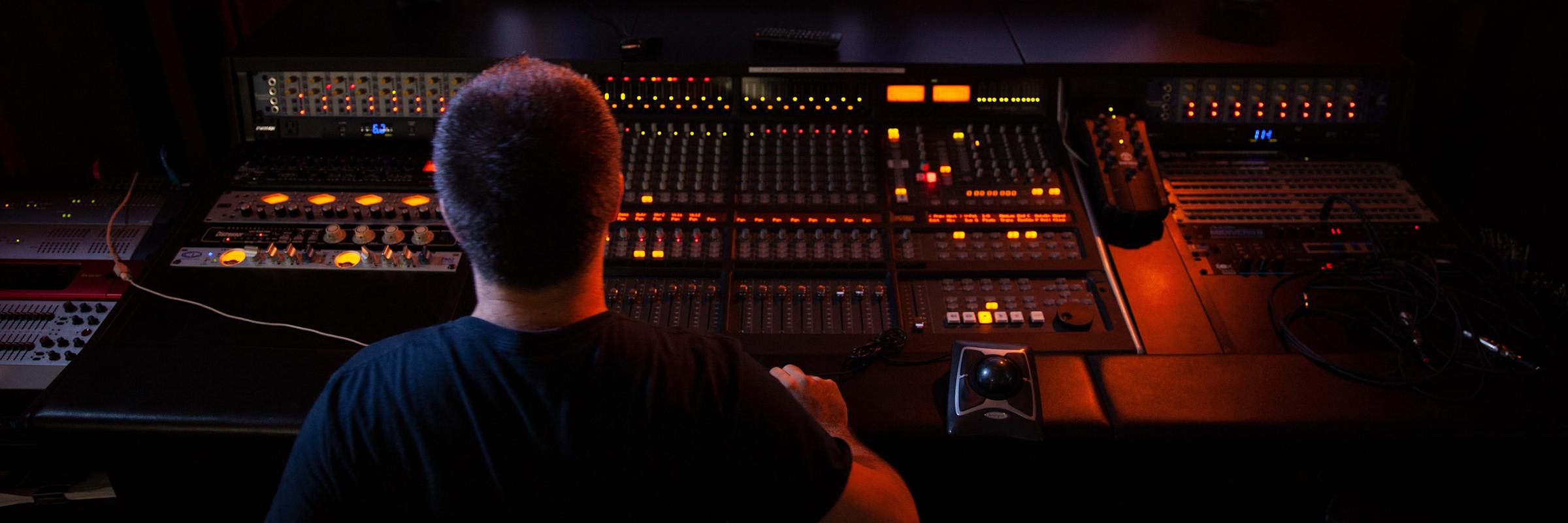 Three students sitting at a sound board in the music studio. 