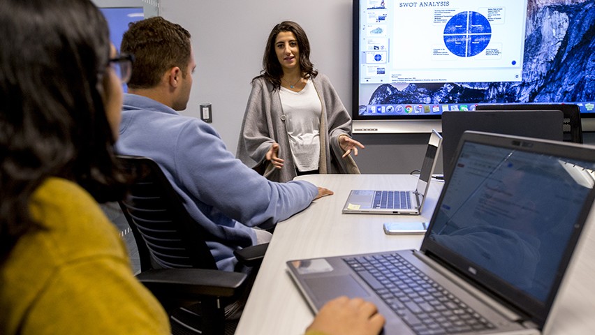 One male and two female students collaborate in a high-tech conference room at Stevens.