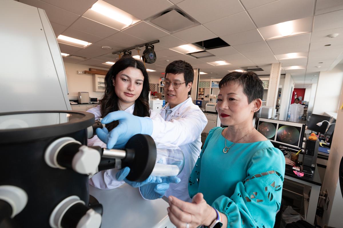 Jennifer Kang-Mieler and two students to her left looking at a slide under a microscope.
