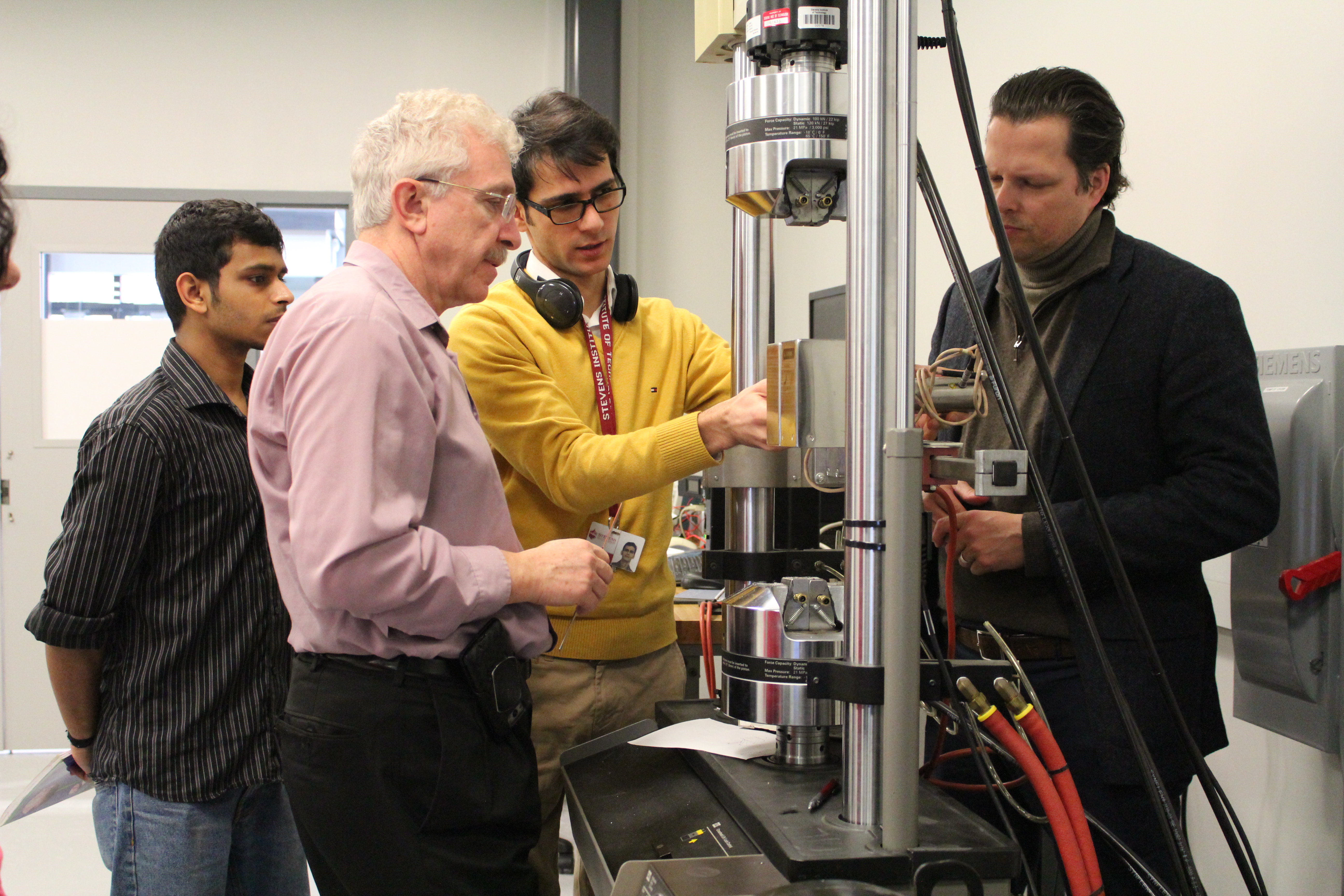 Three male students and a male professor in a lab doing a demonstration on a project