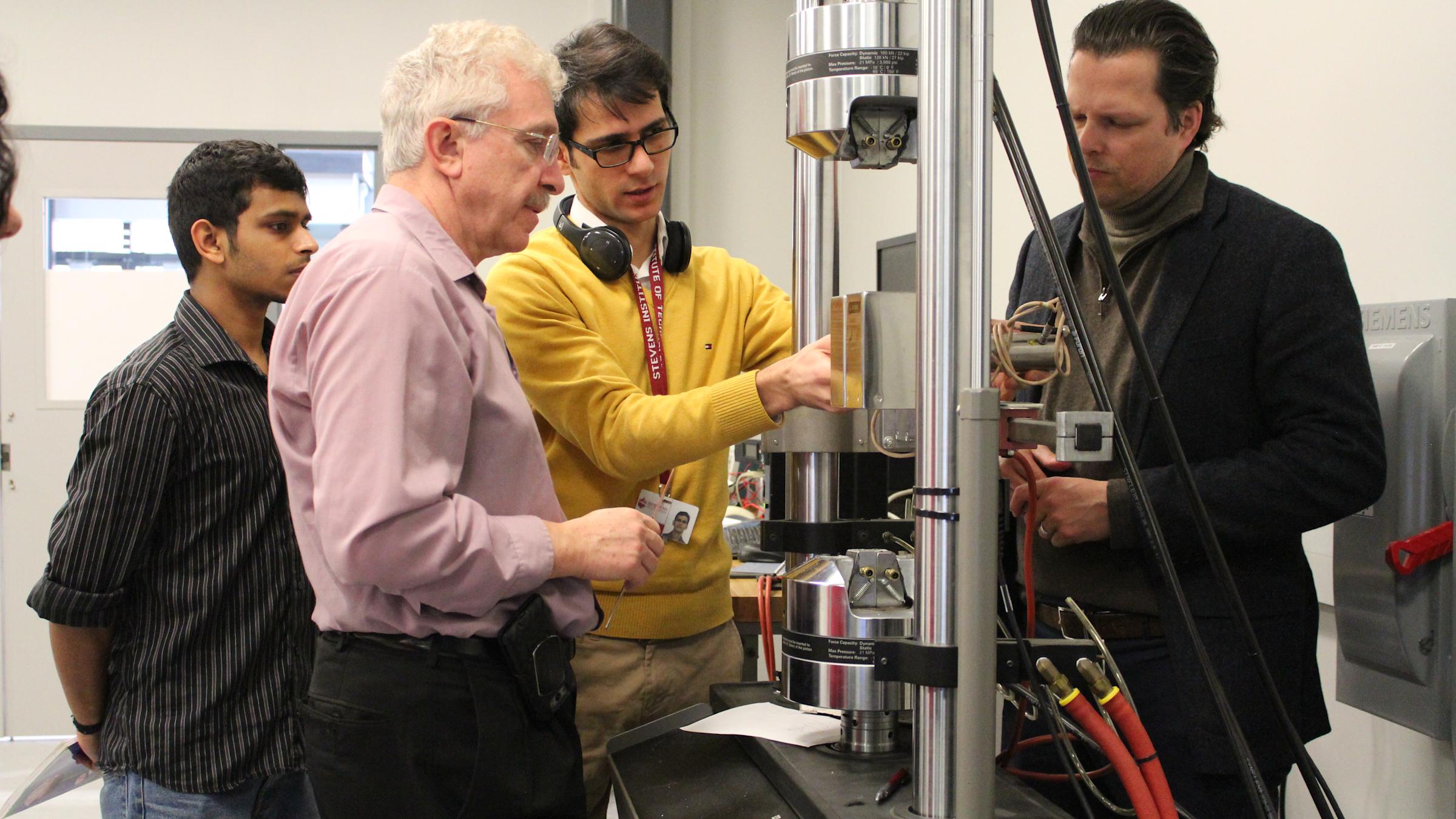 Three male students and a male professor in a lab doing a demonstration on a project