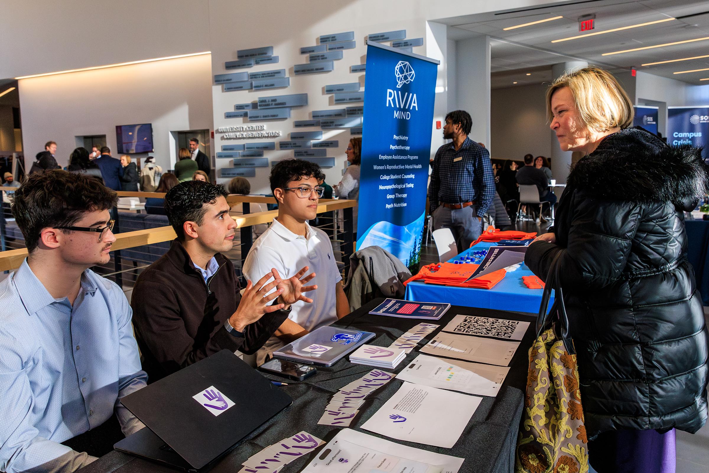 Students sitting at a table talk with a woman.