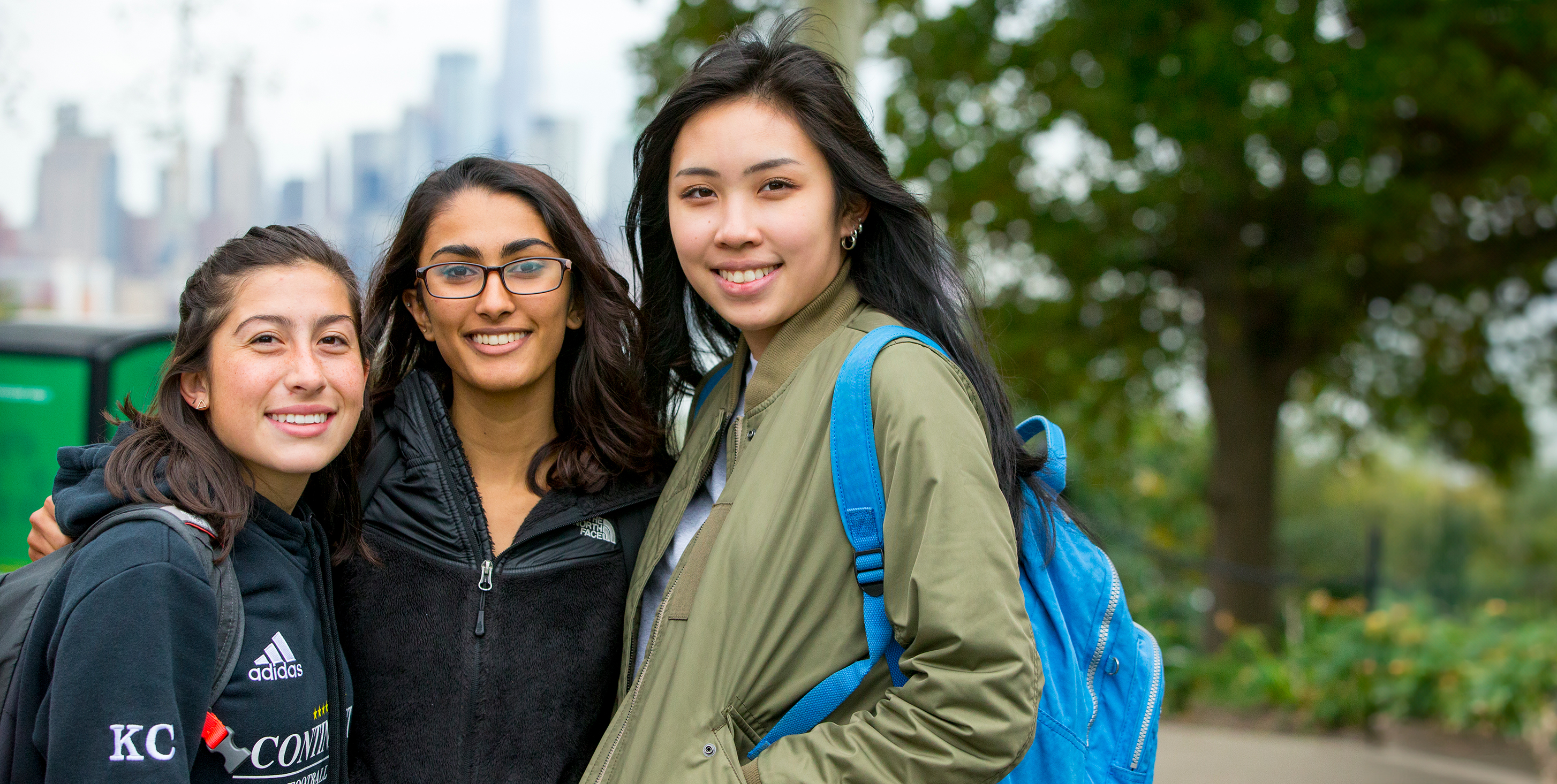 Three female students in the foreground with NYC skyline in the background