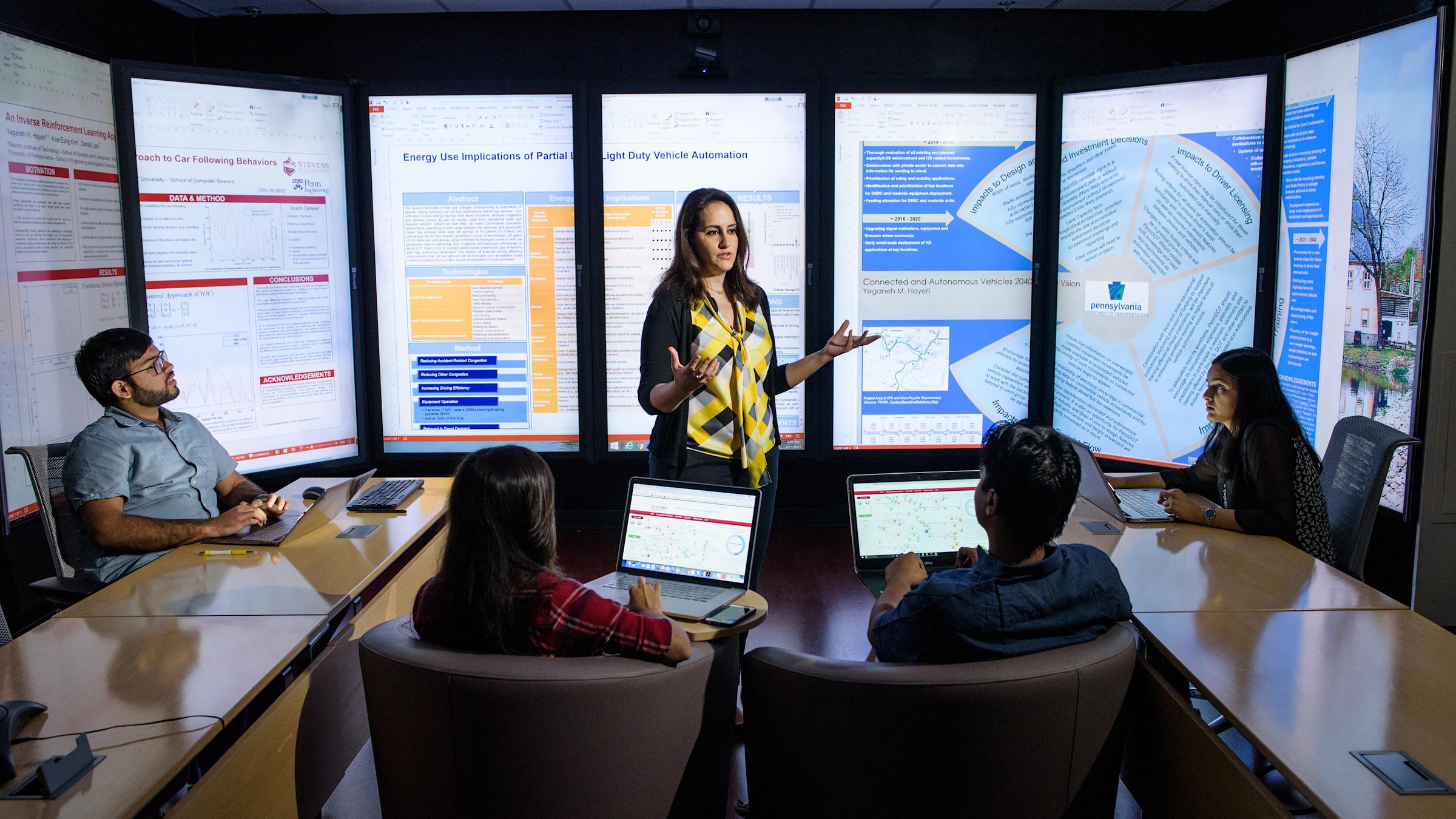 Instructor teaches small class in front of immersion wall of data