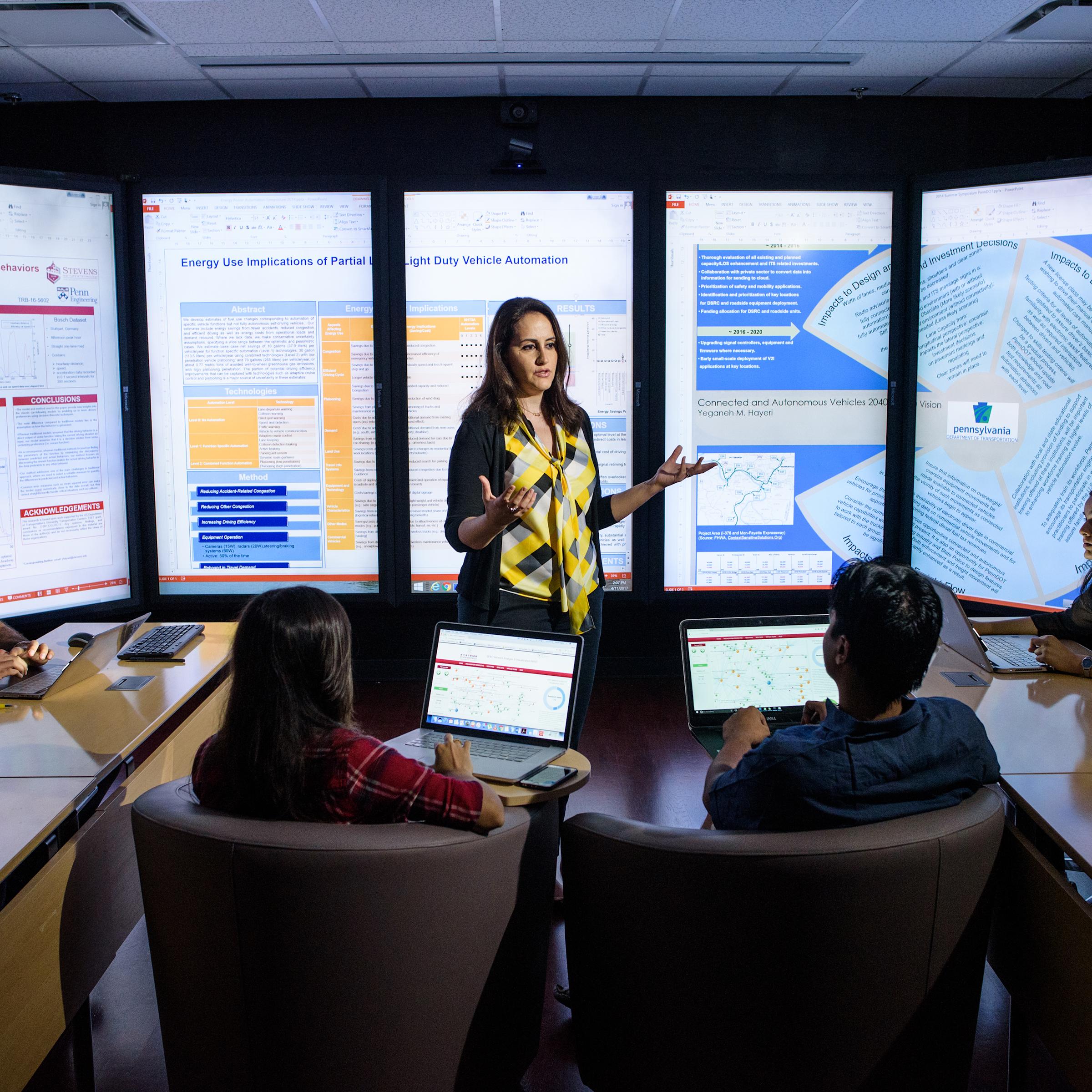 Instructor teaches small class in front of immersion wall of data