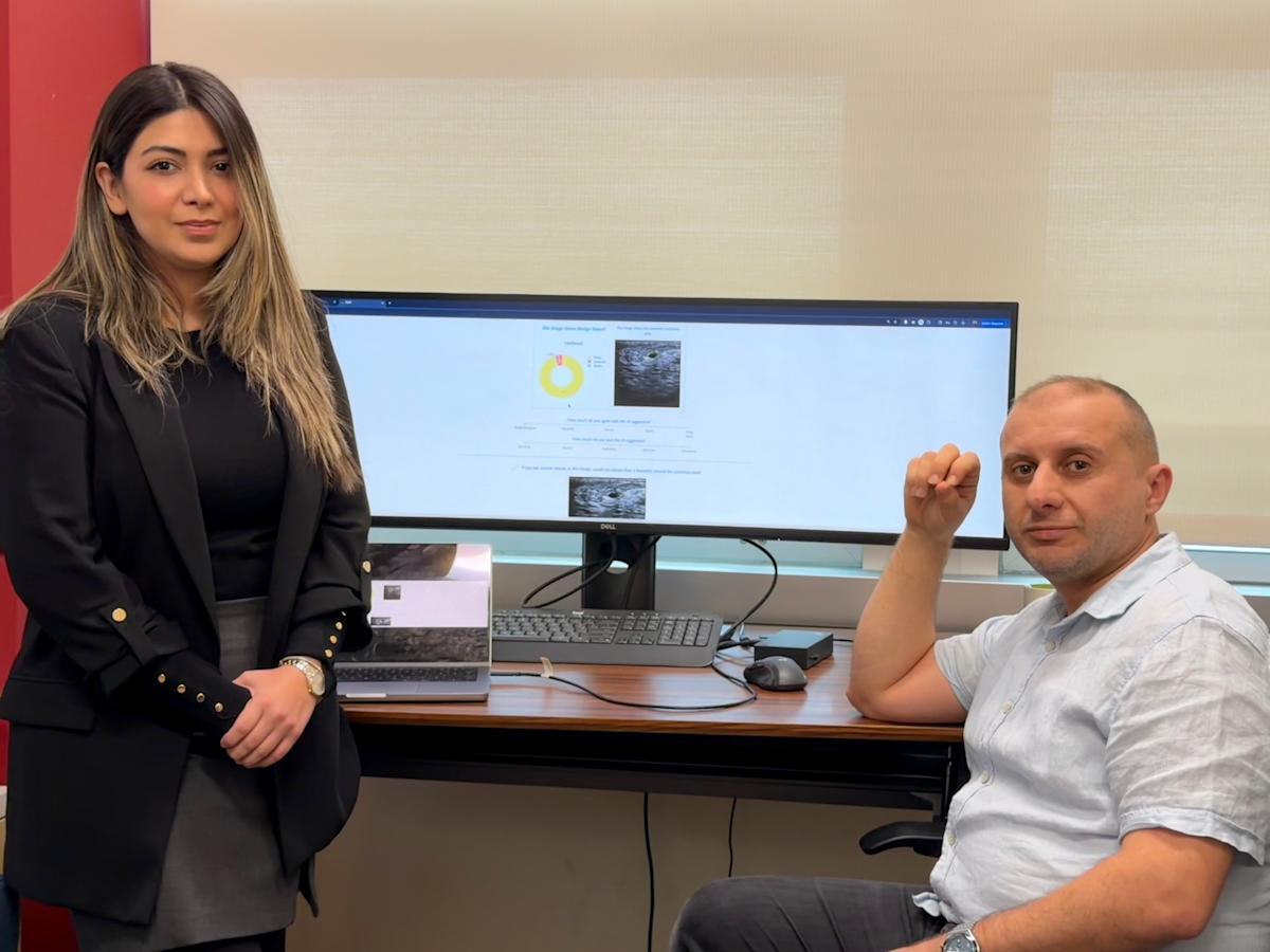Onur Asan sitting in a chair on the left and a Ph.D. student on the write being photographed in front of a computer screen.