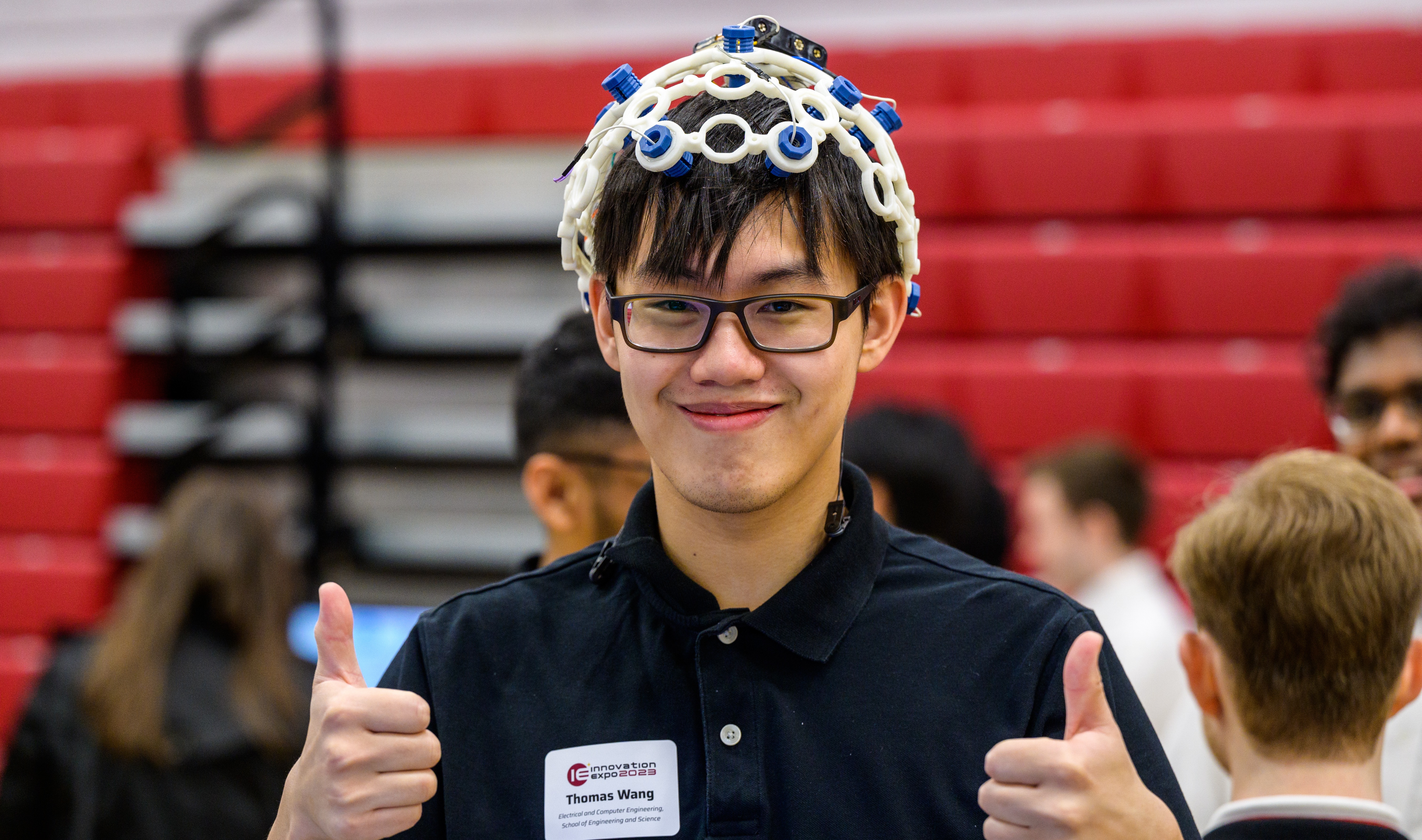 Male student with glasses wearing an experiment on his head with both thumbs up