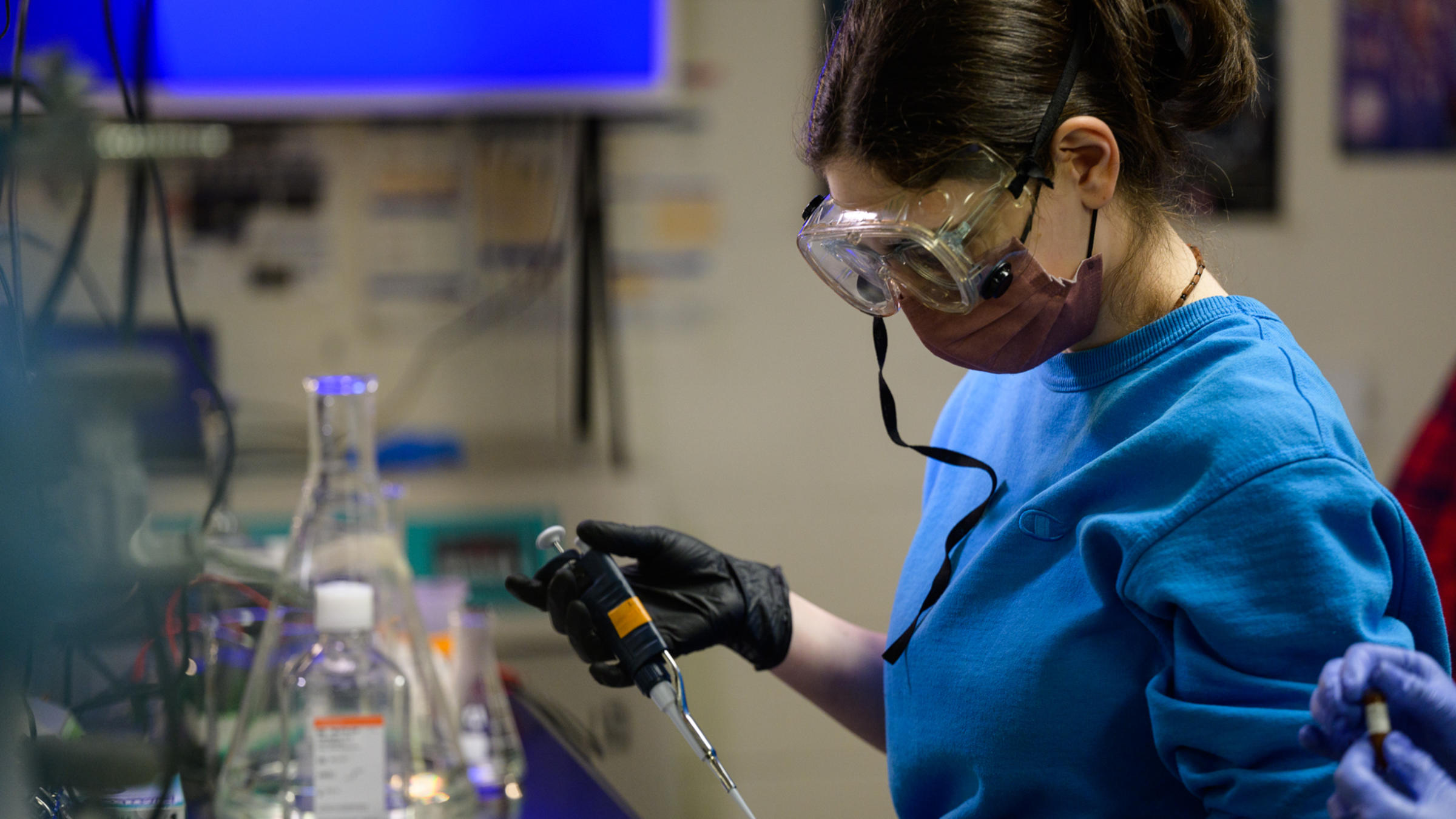 A student wearing safety goggles works with chemical equipment in a lab.