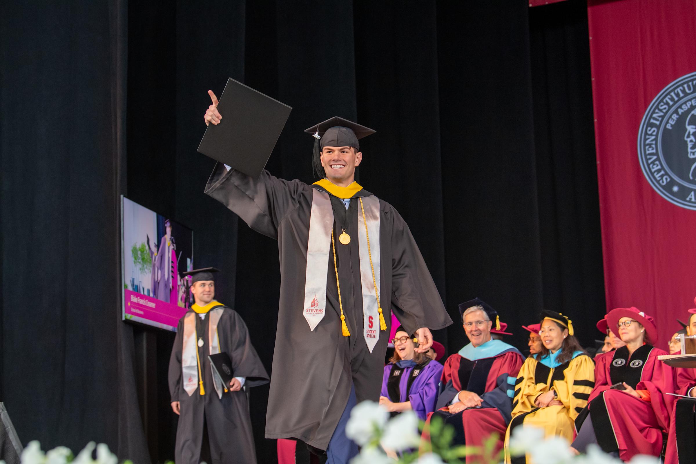 A male graduate of the Class of 2025 walks across stage with his diploma.