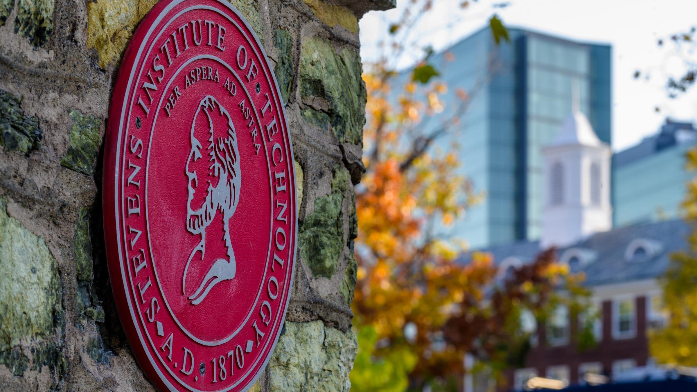 Stevens seal on entrance gate with campus in background