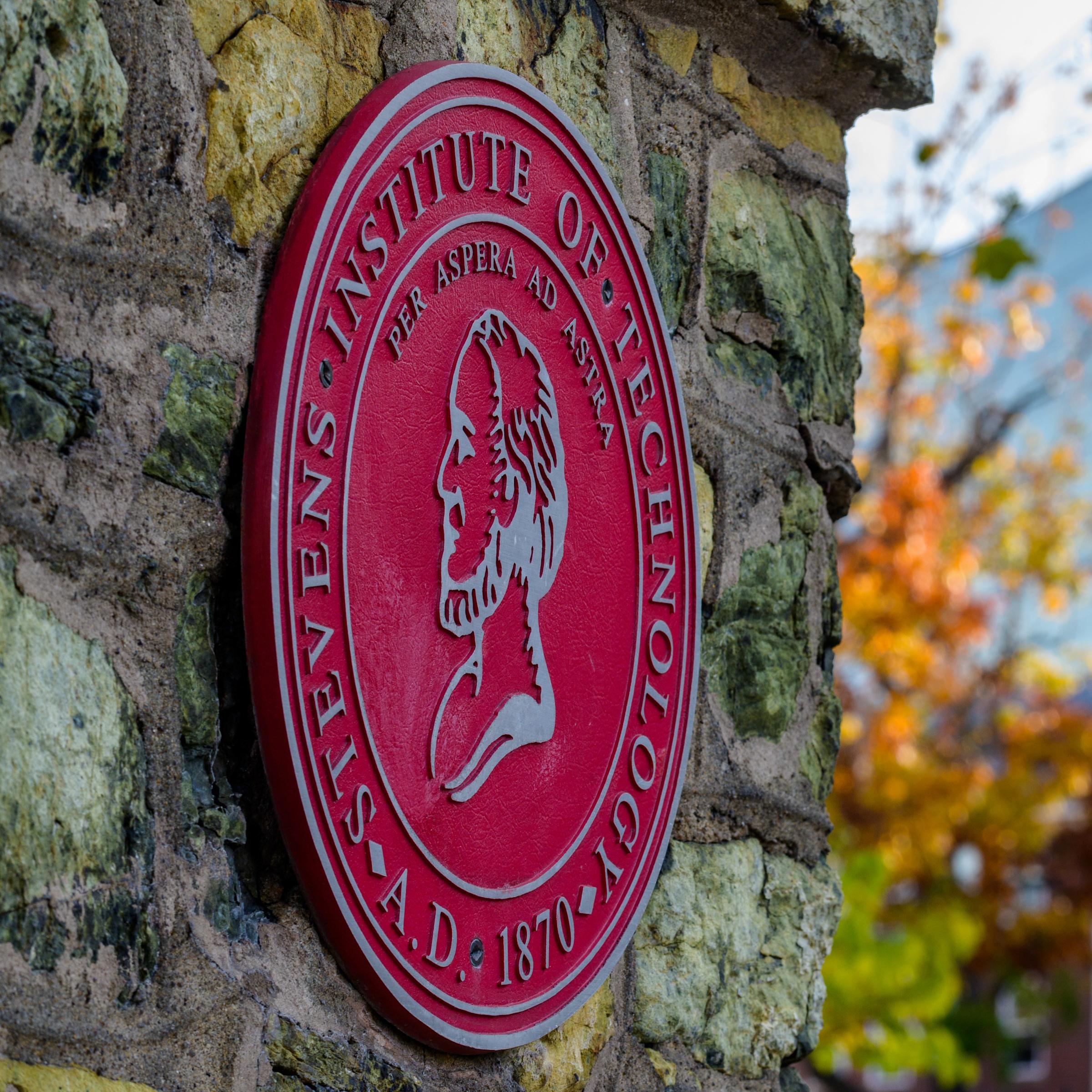 Stevens seal on entrance gate with campus in background
