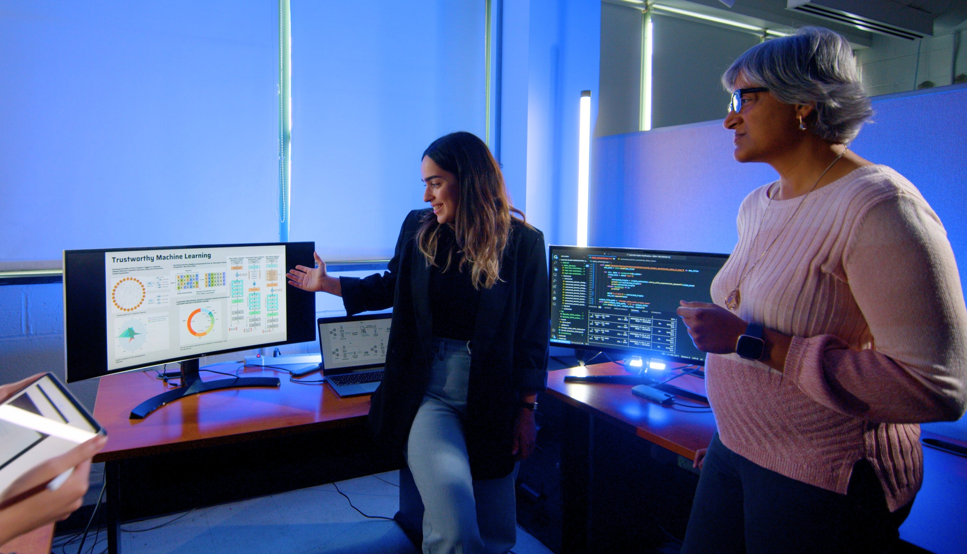 A student and faculty member working with equipment inside of lab lit up in blue light.
