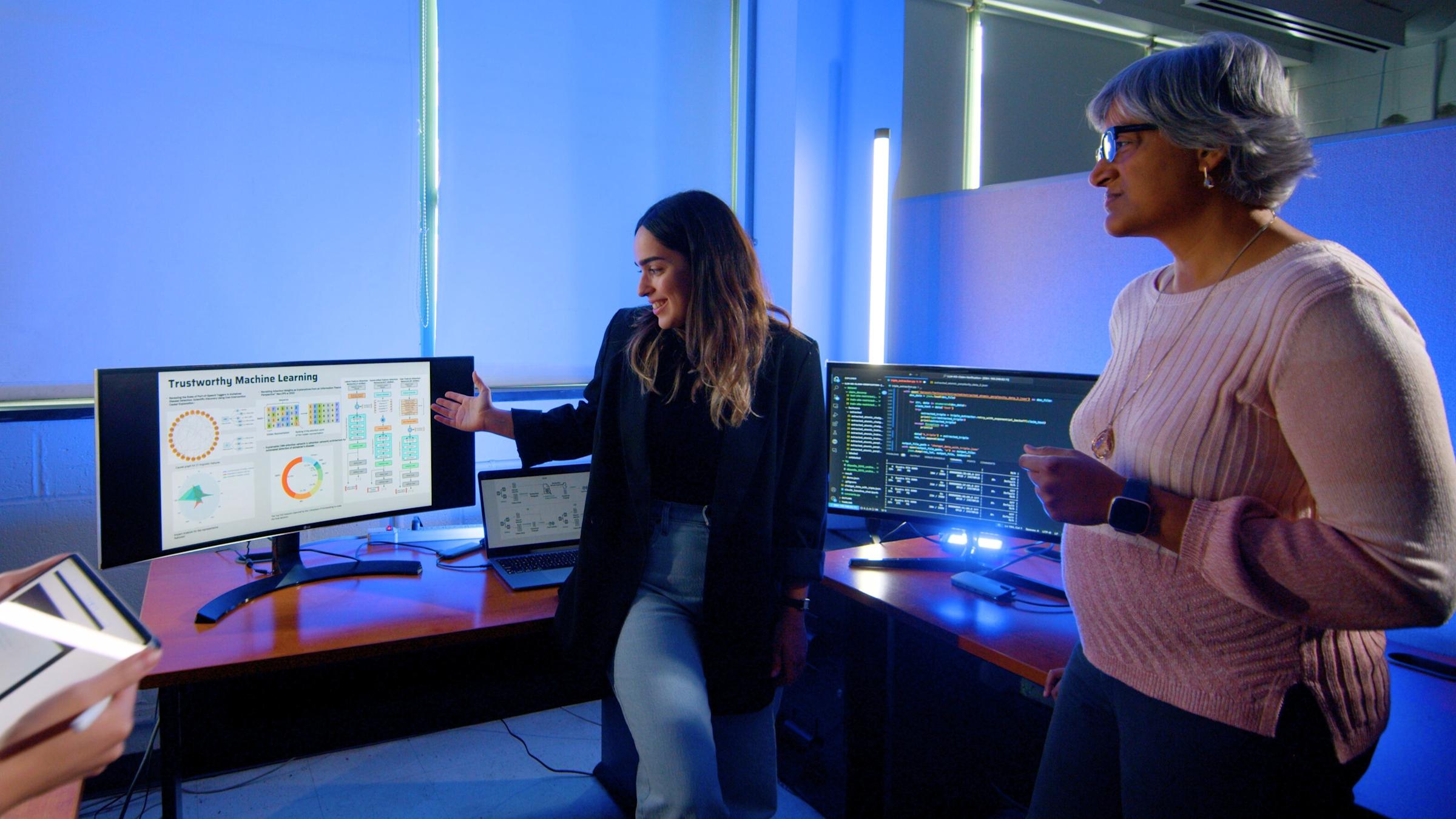 A student and faculty member working with equipment inside of lab lit up in blue light.