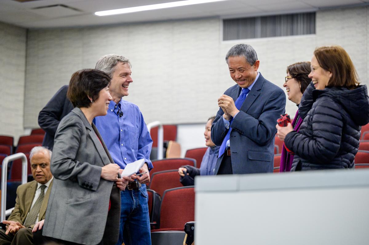 Group of five people stand talking and laughing together in an auditorium