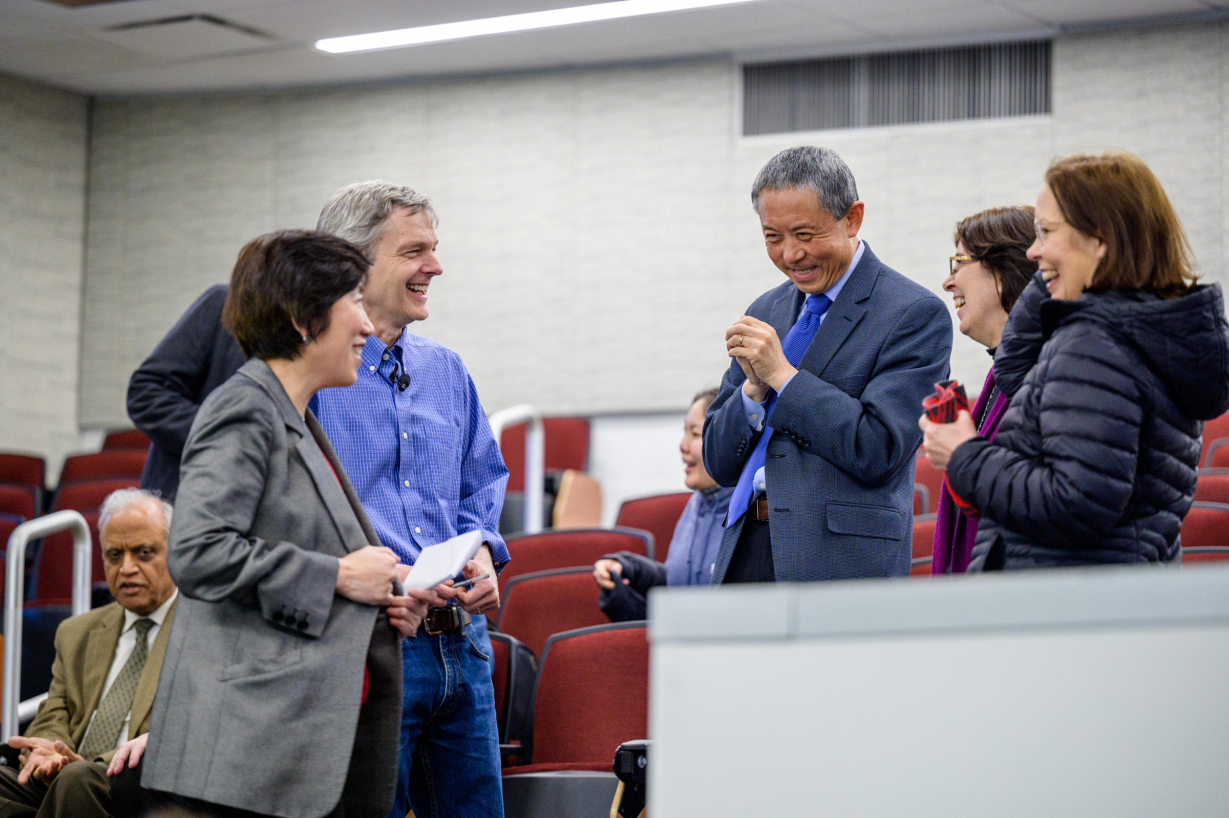 Group of five people stand talking and laughing together in an auditorium