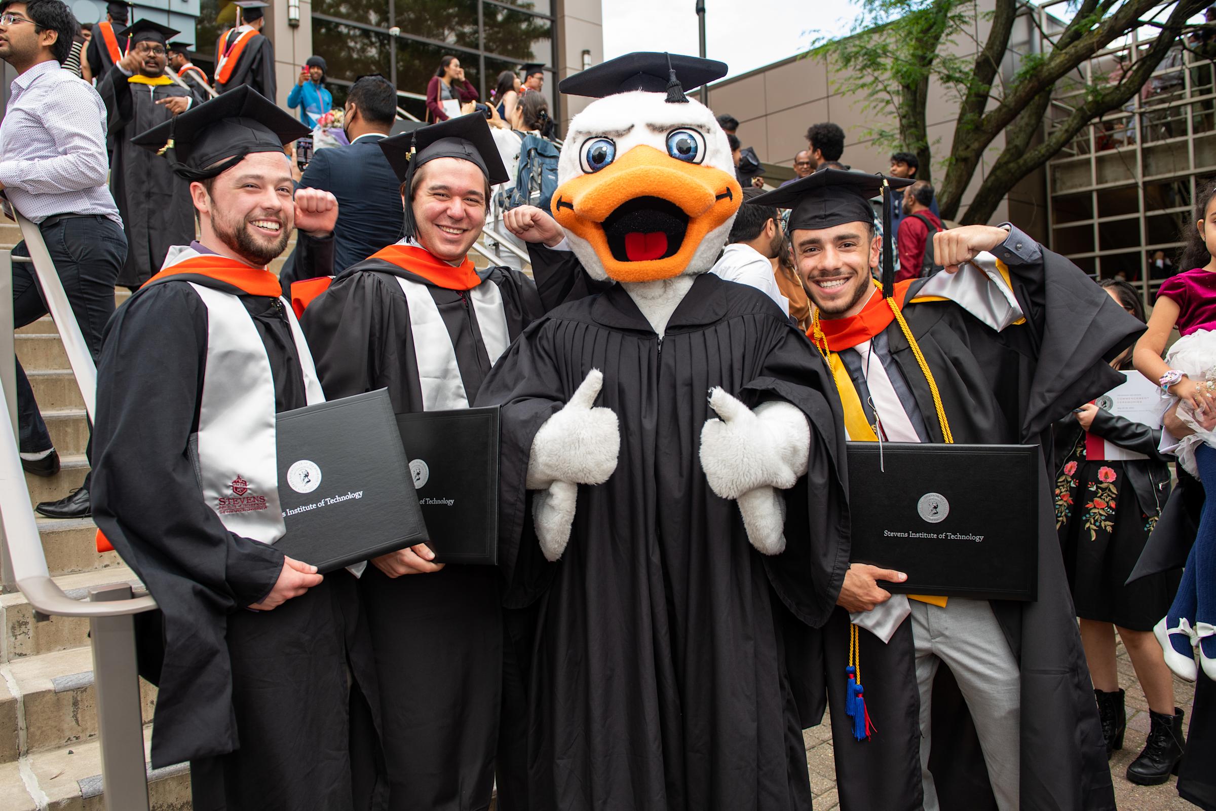Three students pose with Attila in Commencement attire