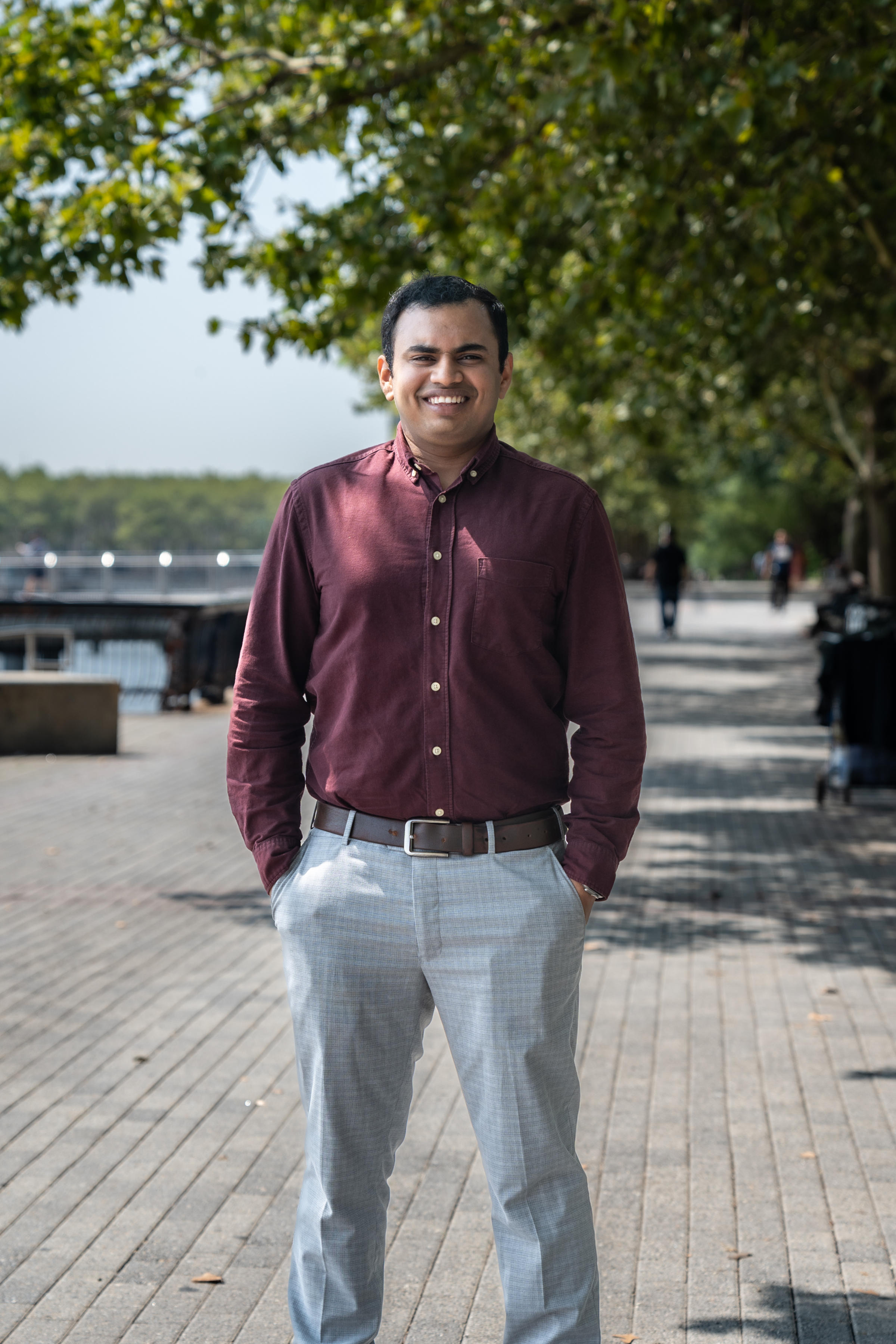 Mani stands with Hoboken's riverwalk in the background on a sunny day.