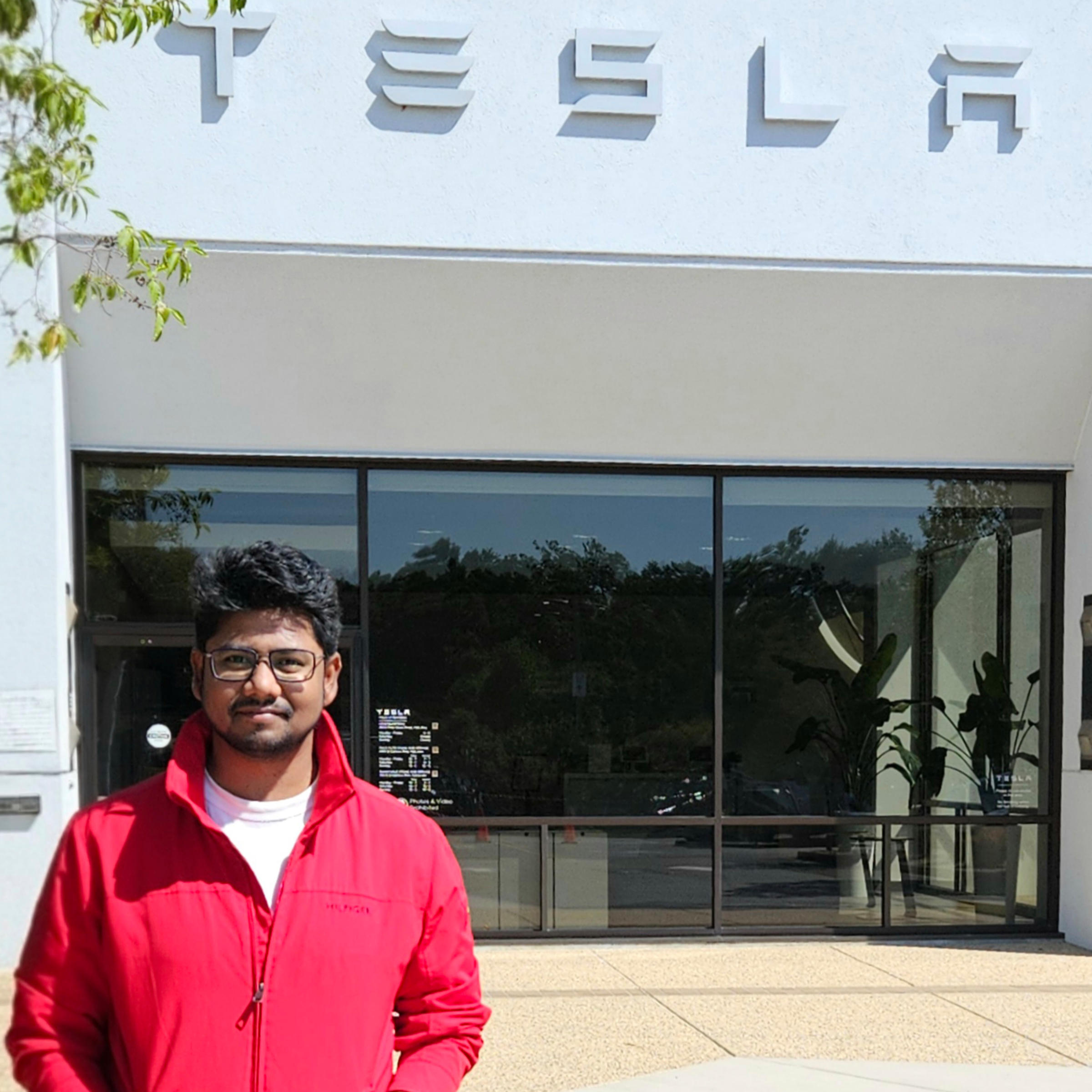A man in a red hoodie poses in front of Tesla's office.