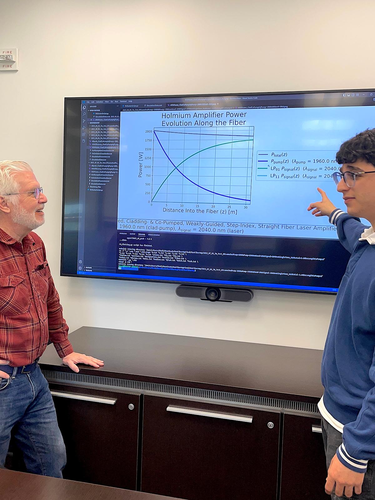 A photo of Ed Whittaker and Khalid Musa talking in front of a big screen with physics equations