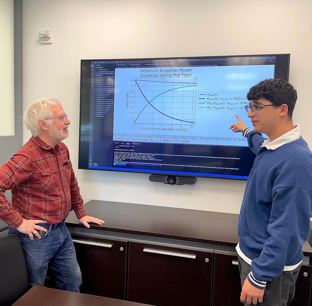 A photo of Ed Whittaker and Khalid Musa talking in front of a big screen with physics equations