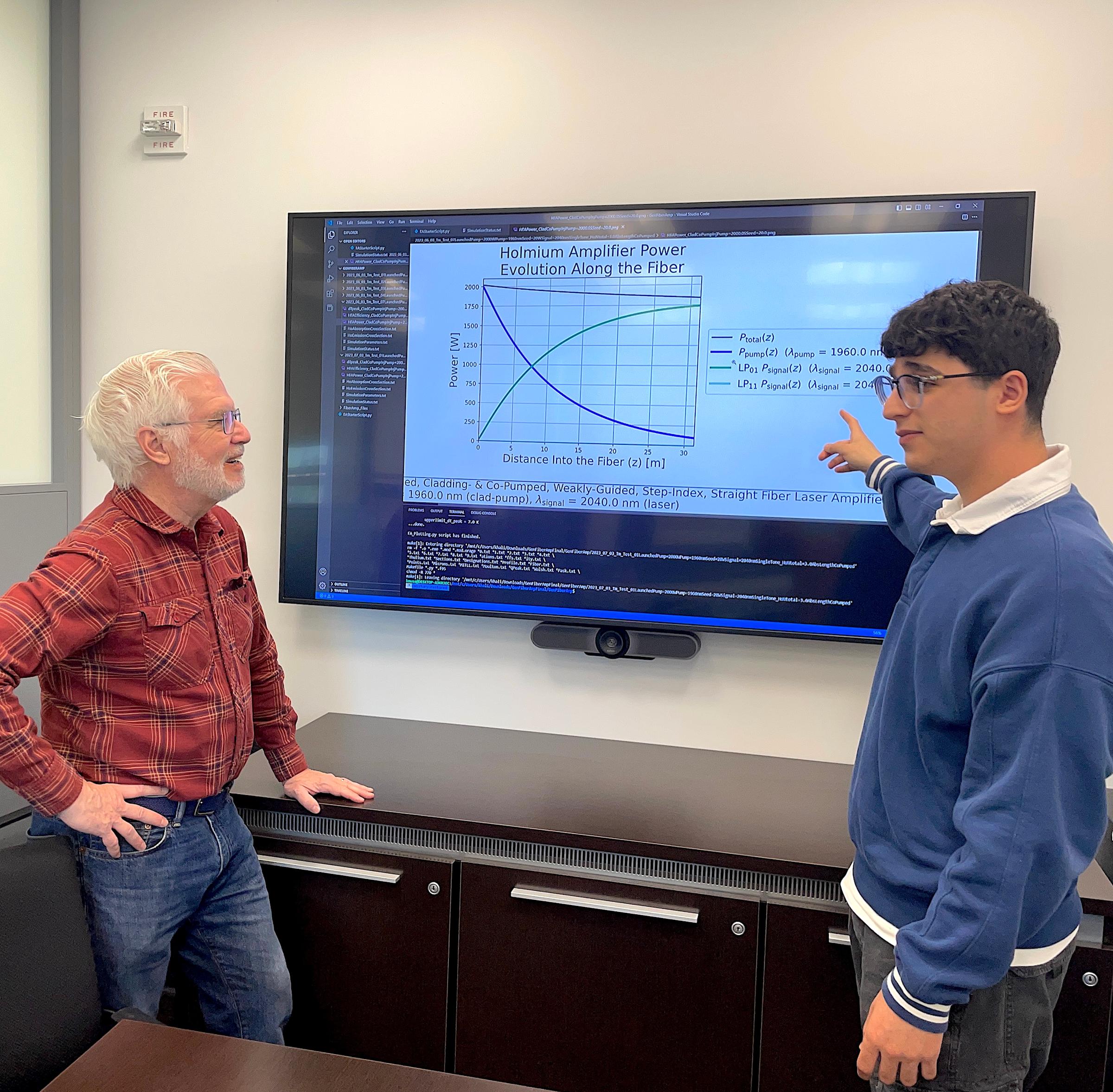 A photo of Ed Whittaker and Khalid Musa talking in front of a big screen with physics equations