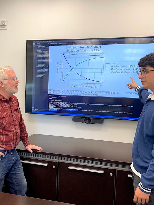 A photo of Ed Whittaker and Khalid Musa talking in front of a big screen with physics equations