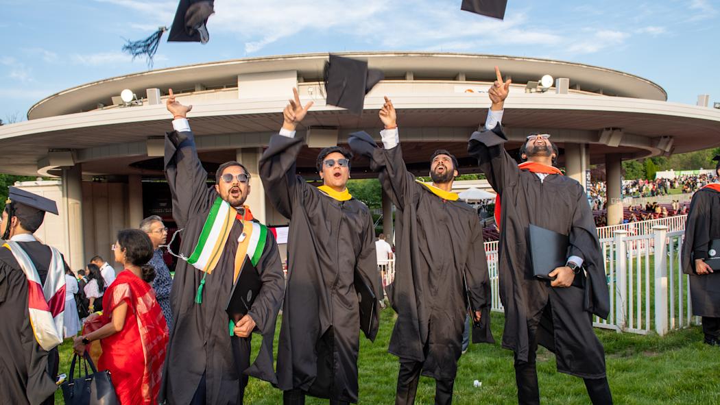 A group of graduates in regalia toss their caps