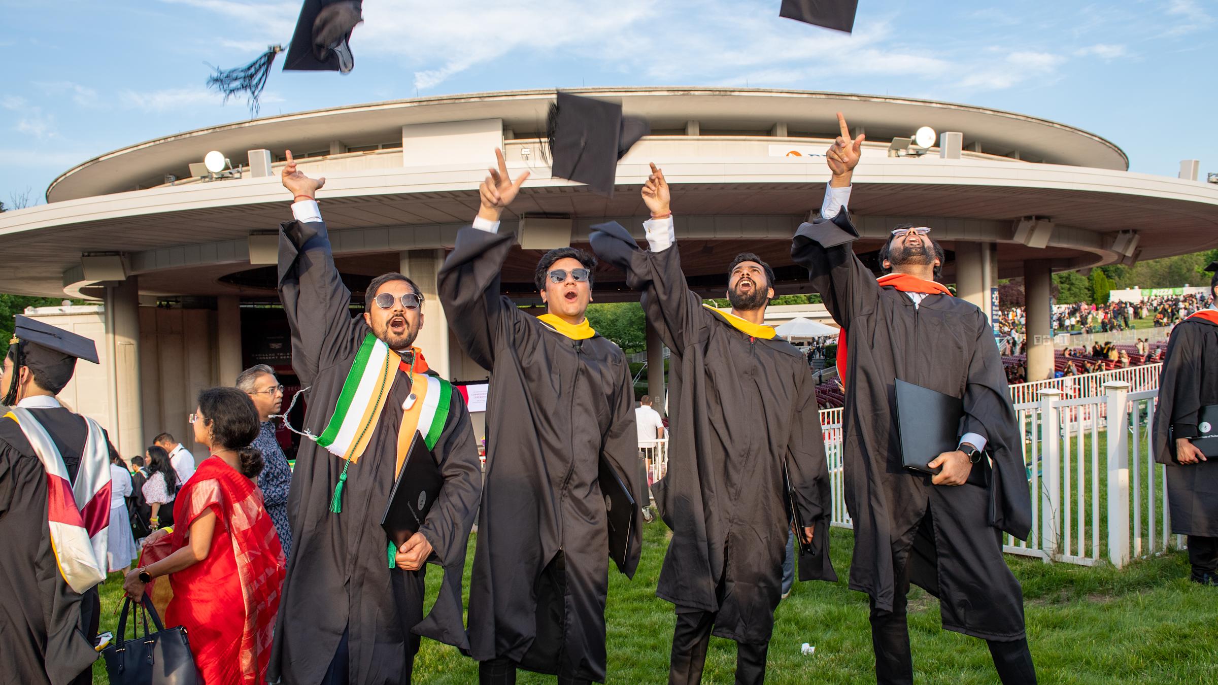 A group of graduates in regalia toss their caps