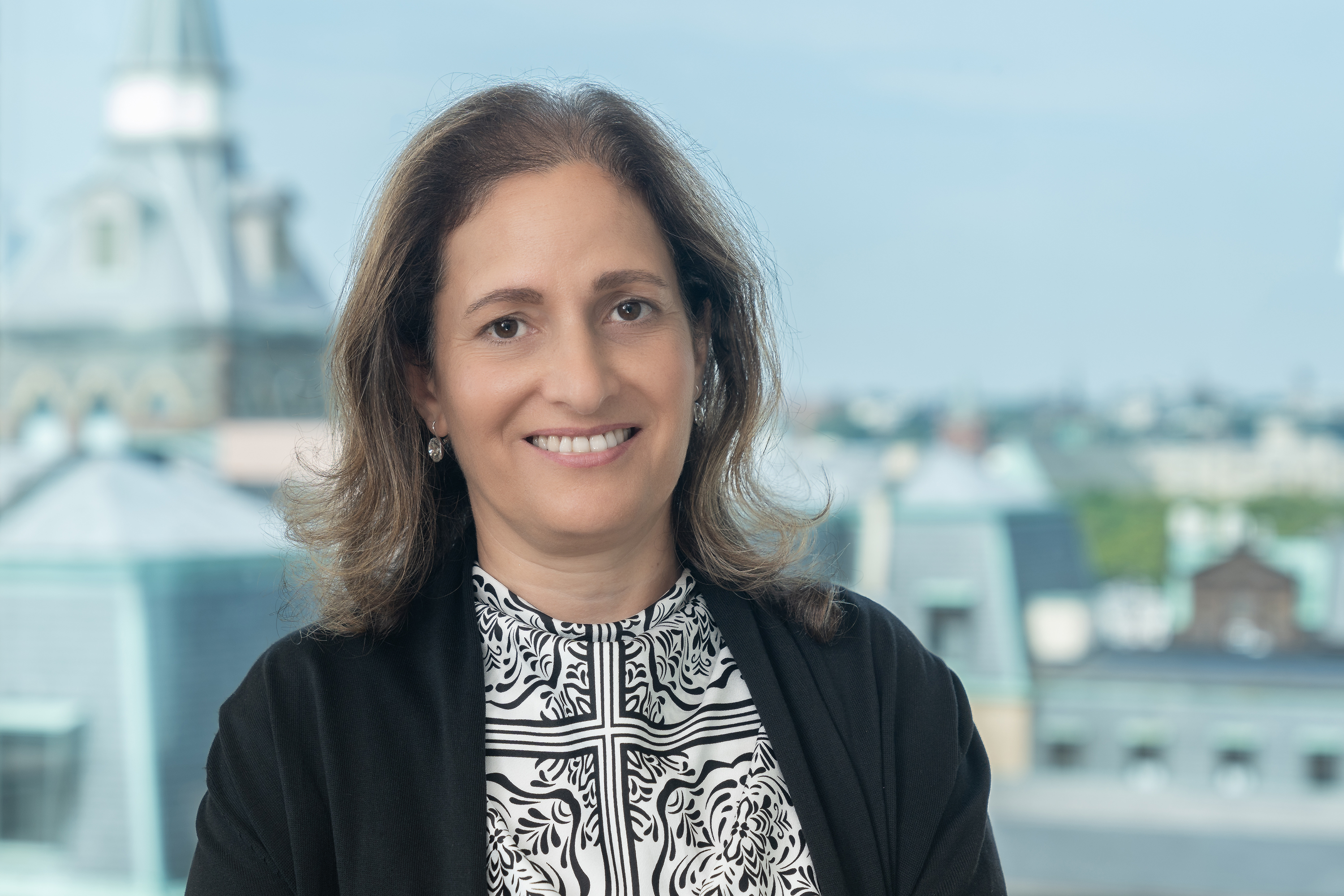 Dr. Joelle Saad-Lessler stands in front of a window with the New York City skyline in the background.