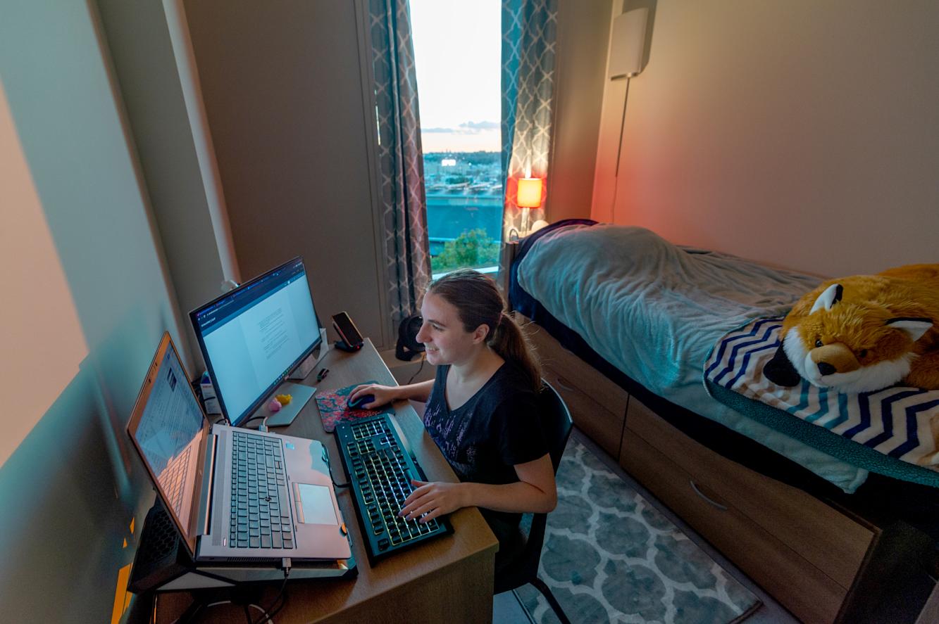 Student cheerfully types on her laptop while stuffed fox looks on.