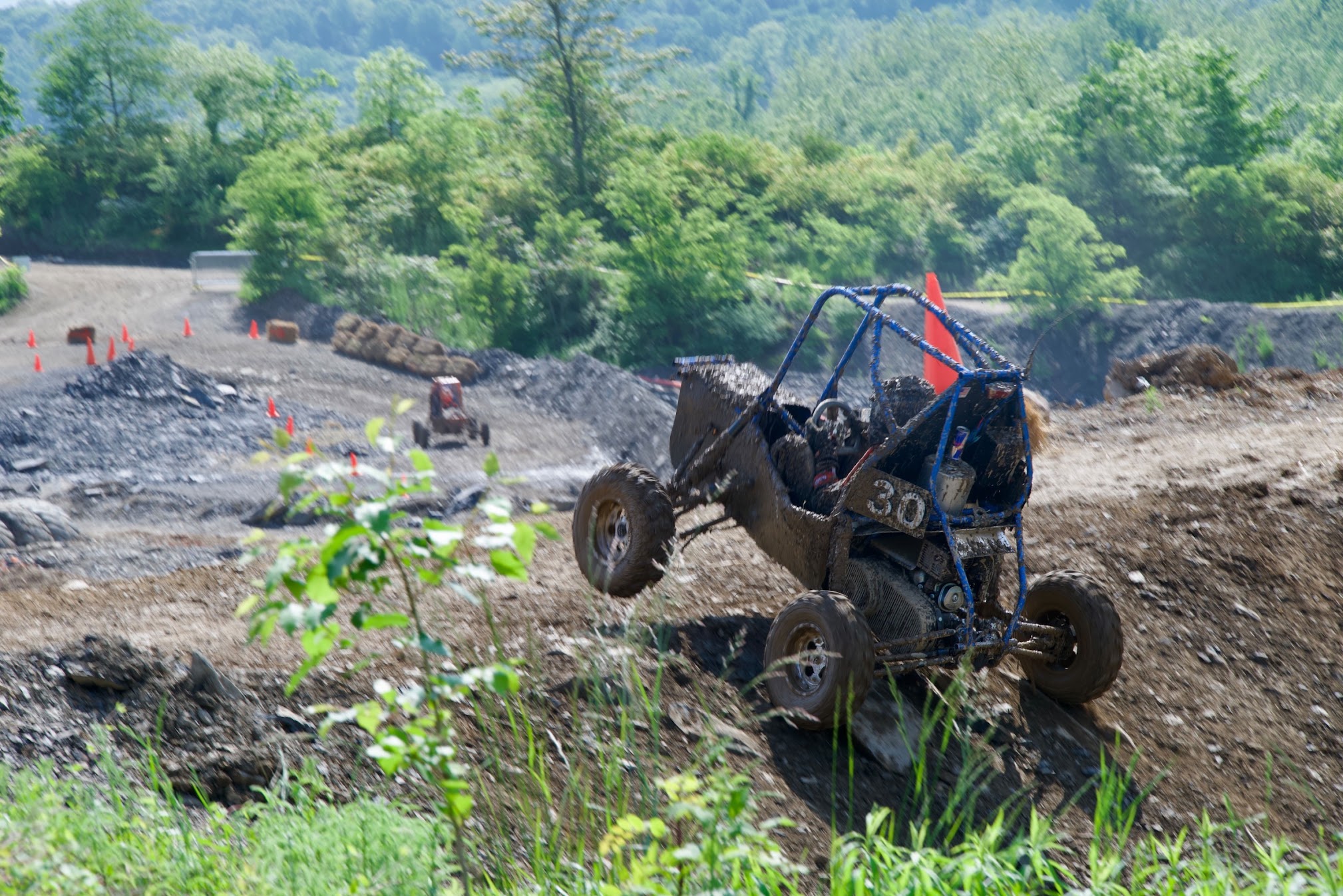 Photo of an off-road vehicle going over a muddy terrain, with green trees in the background