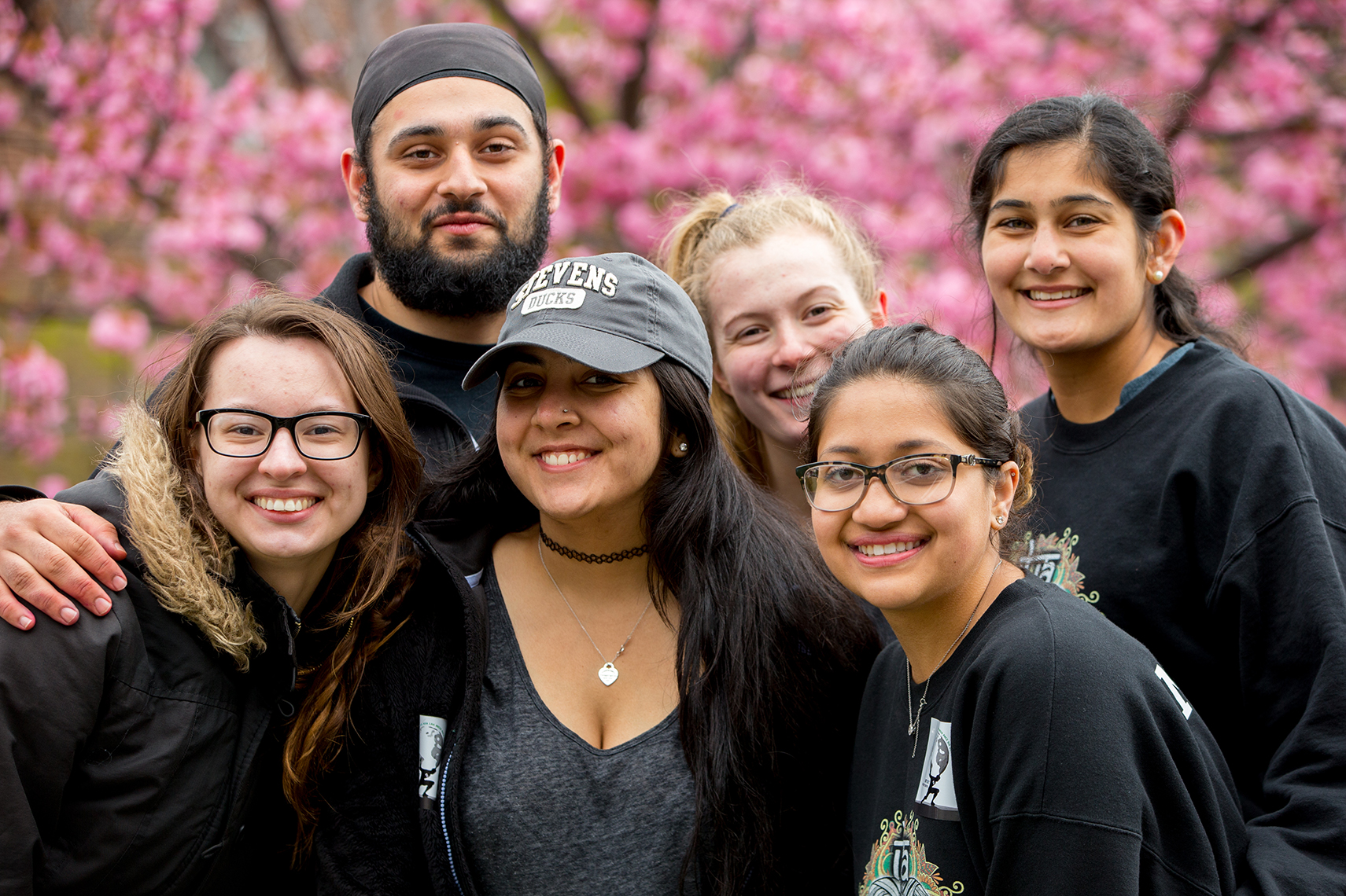 Six students smiling in front of trees with flowers