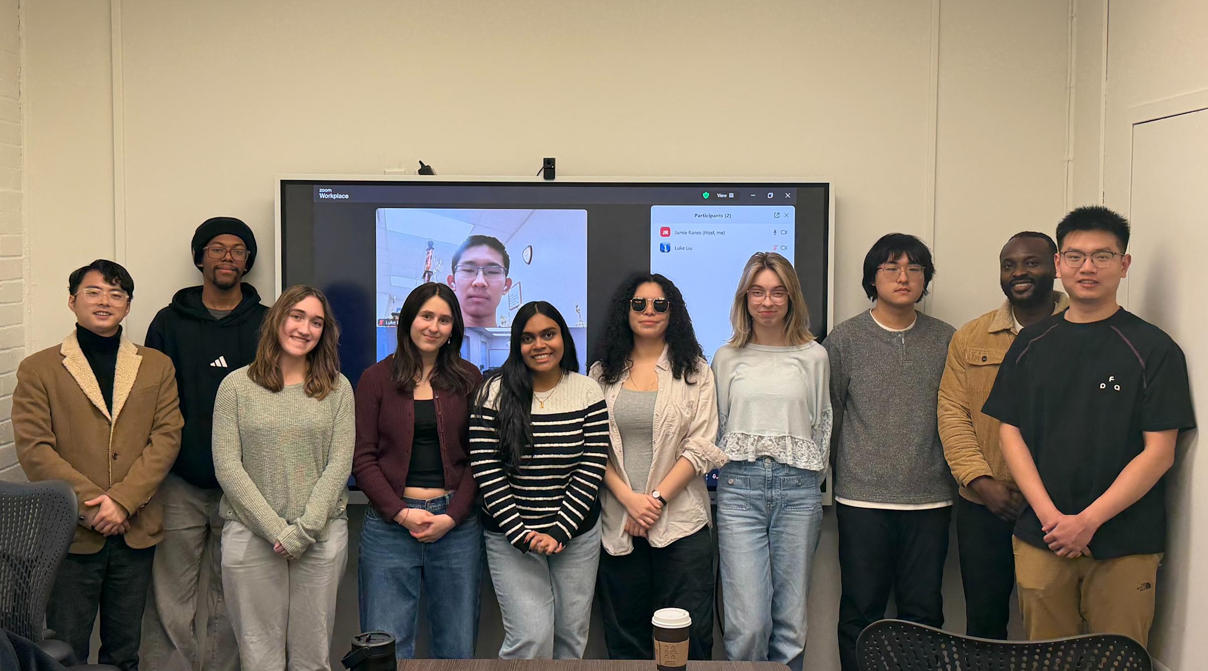 Jia Mi (at left) stands with his winning 2026 MECC team: Sie Salandy-Smith, Brianna Schaad, Zora Swindell, Disha Rana, Emily Lossman, Jamie Ranes, Yubo Wang, Samuel Boamah and Kaiqi Zhao, and (on screen) Luke Liu from Lone Star College.