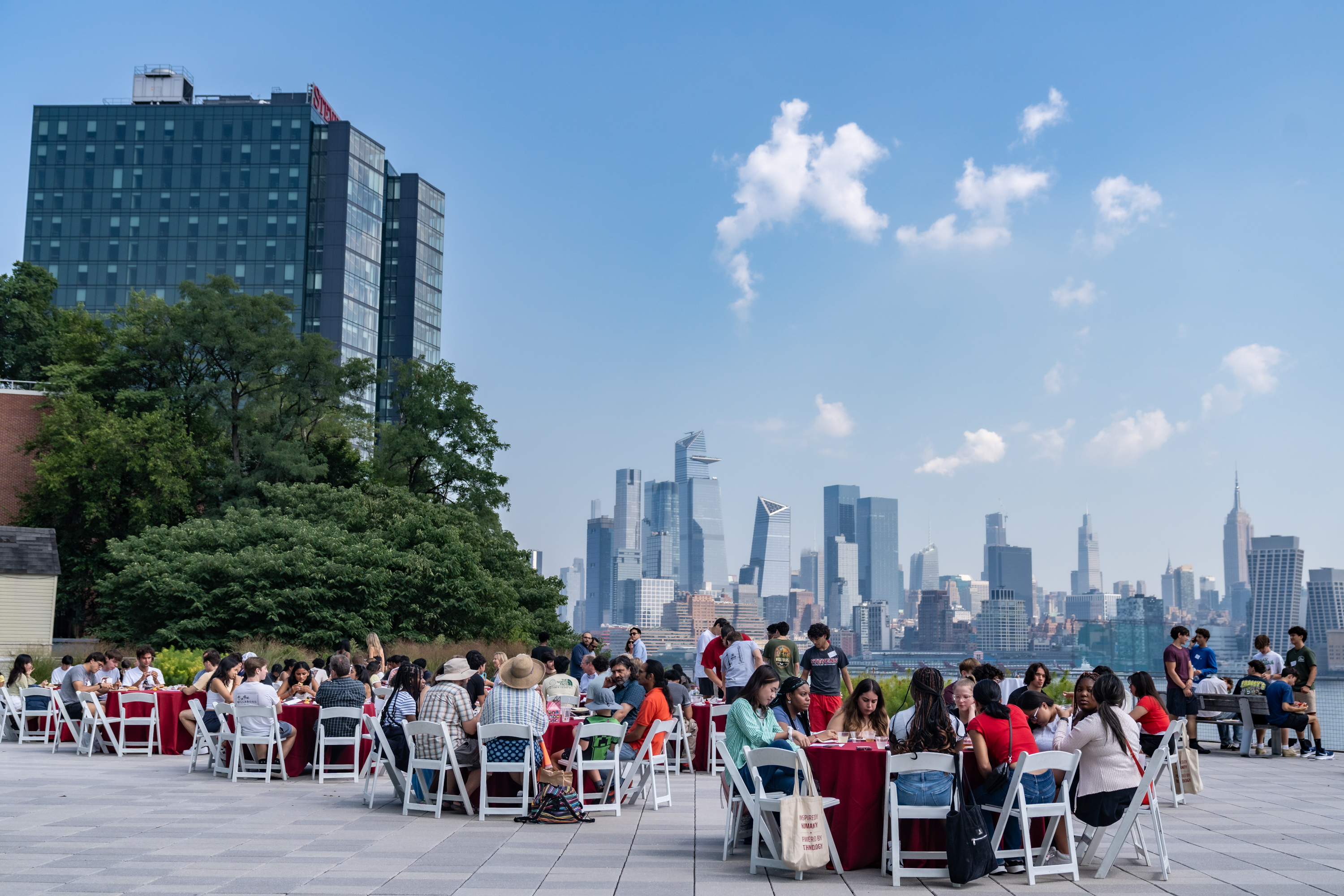Students sitting at tables eating lunch with the New York City skyline in the background.