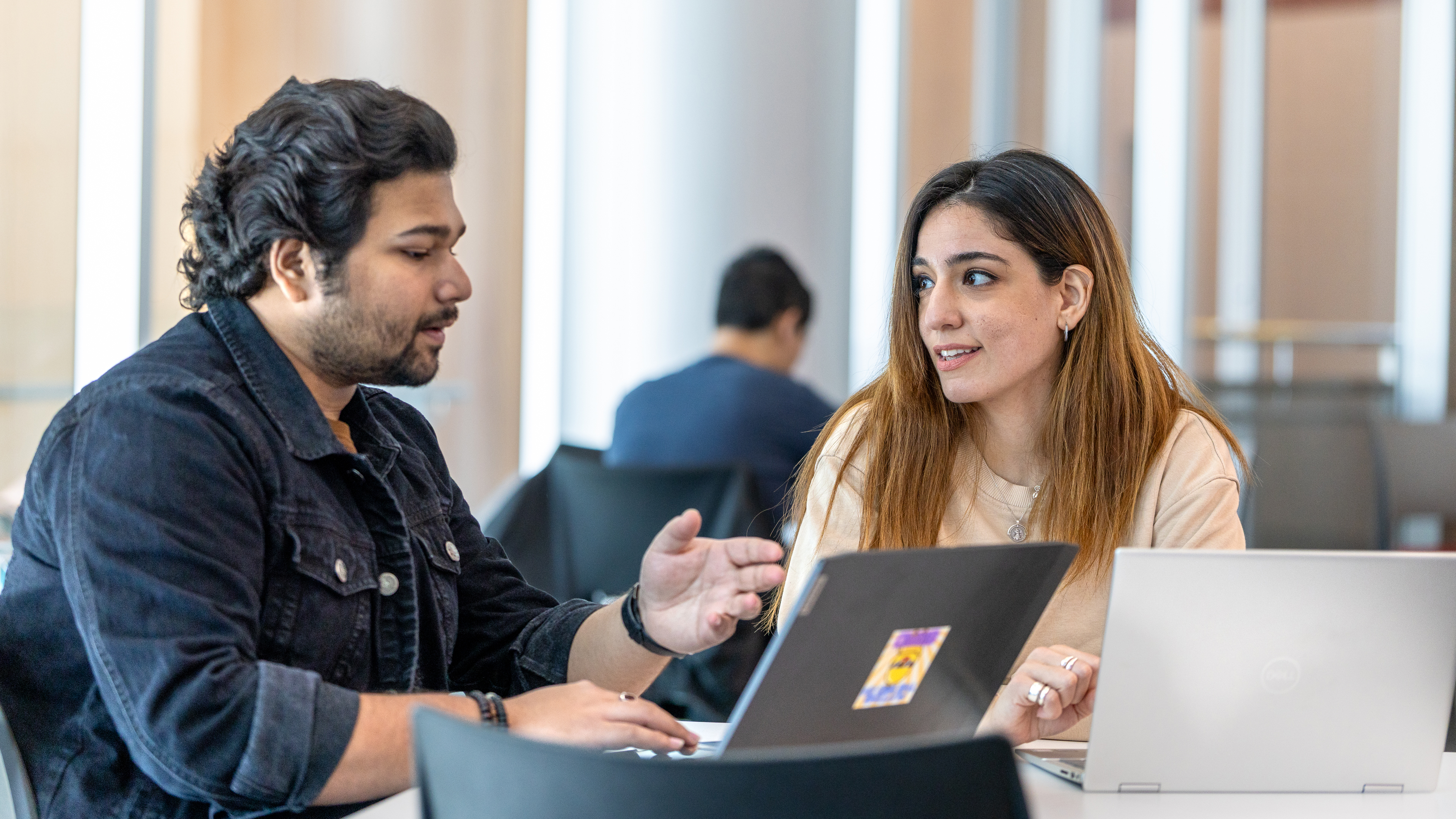 Two graduate students converse in front of their laptops.