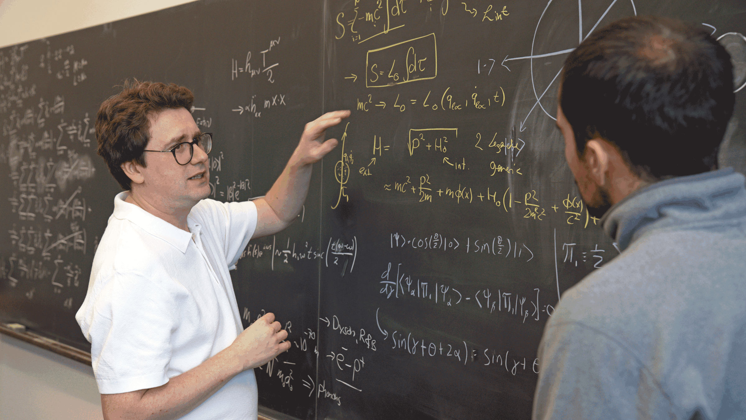 Stevens physics Ph.D. student Christos Karapoulitidis (right) watches Igor Pikovski explain theories via a chalkboard.