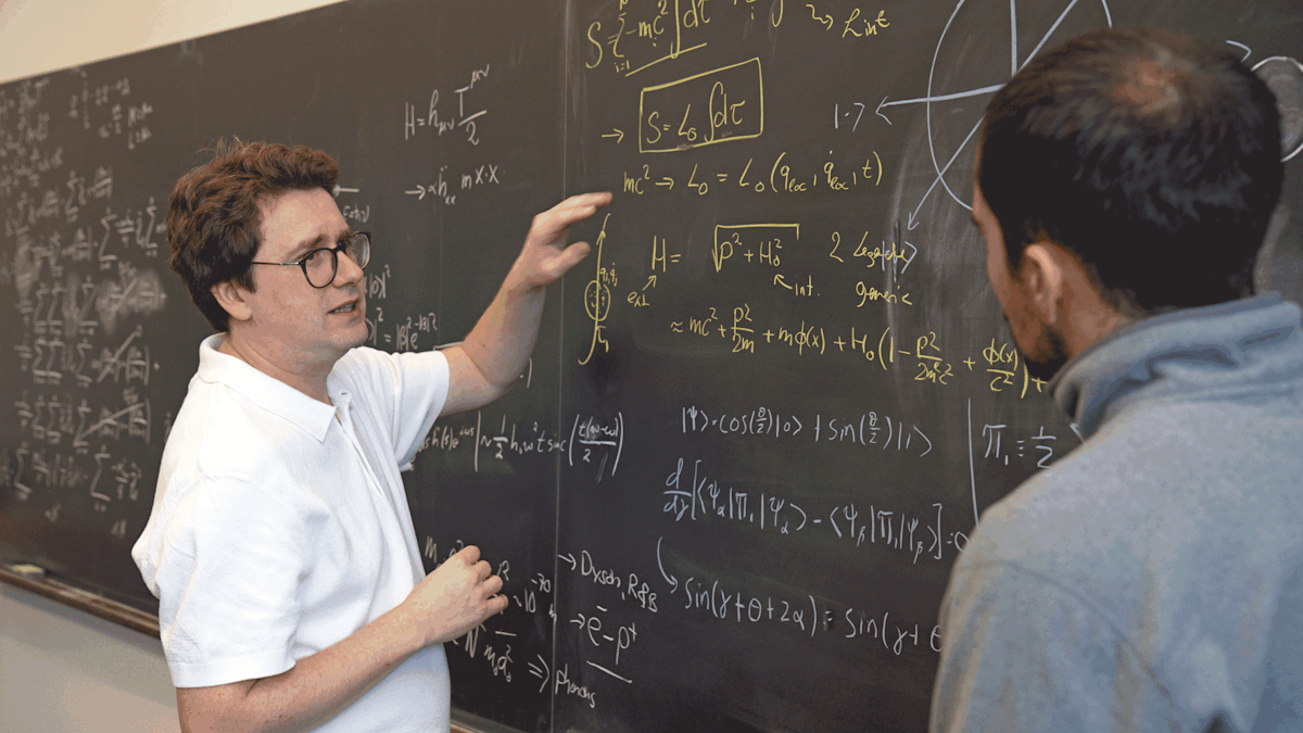 Stevens physics Ph.D. student Christos Karapoulitidis (right) watches Igor Pikovski explain theories via a chalkboard.